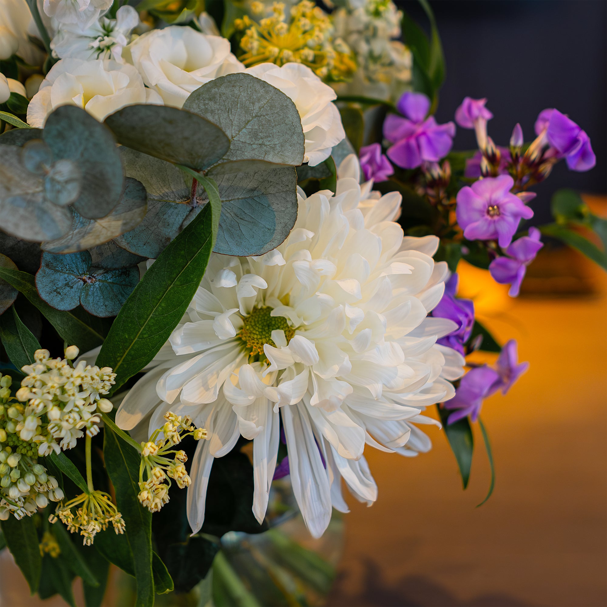 This is a close-up view of a bespoke floral arrangement for the Pan Pacific corporate event. It highlights a mix of white chrysanthemums, purple accents, eucalyptus, and lush foliage - event floristry by Amaranté London.