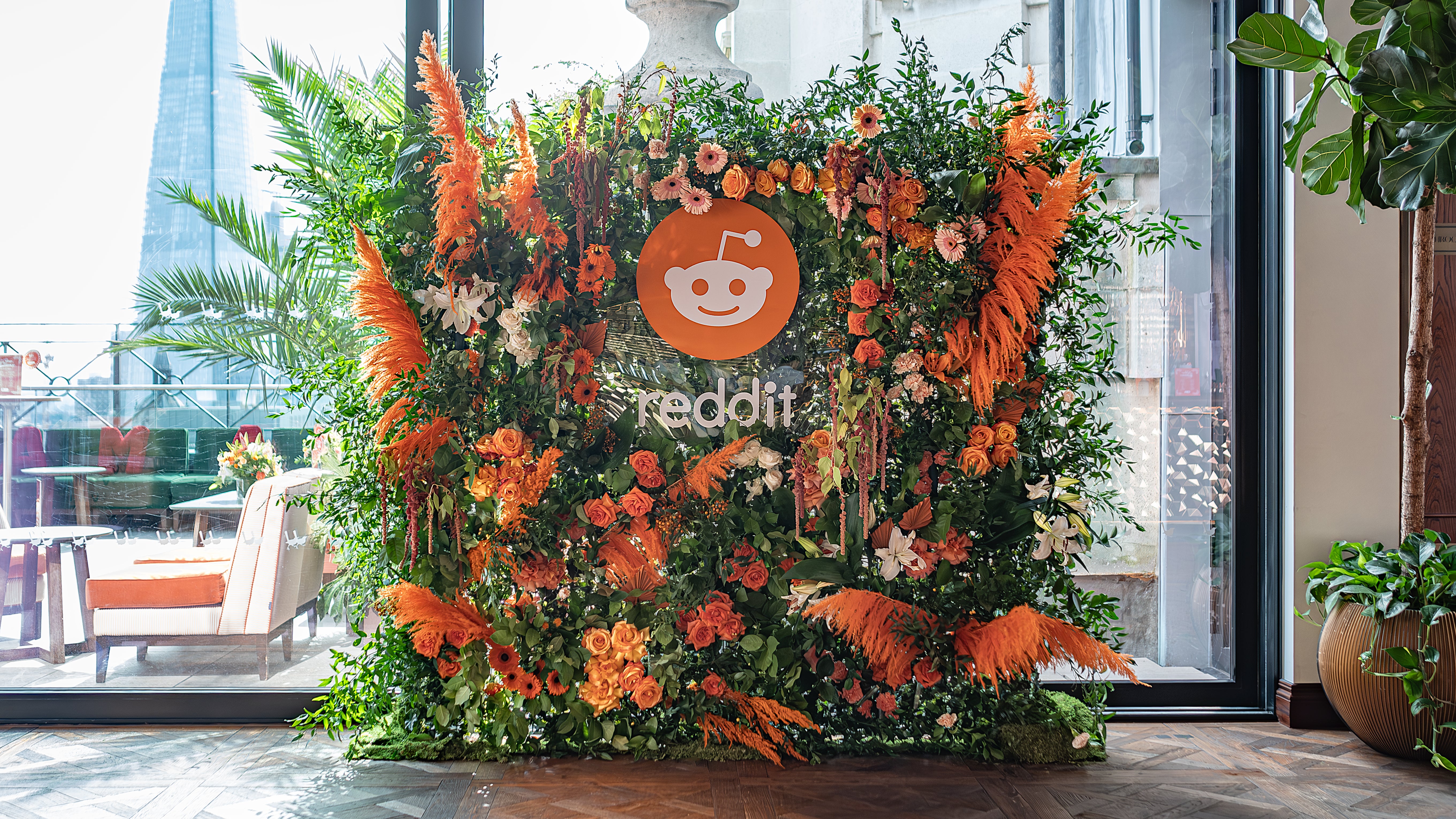Vibrant orange and green bespoke floral wall installation by Amaranté, designed for Reddit's event, showcasing their brand colours in full bloom.