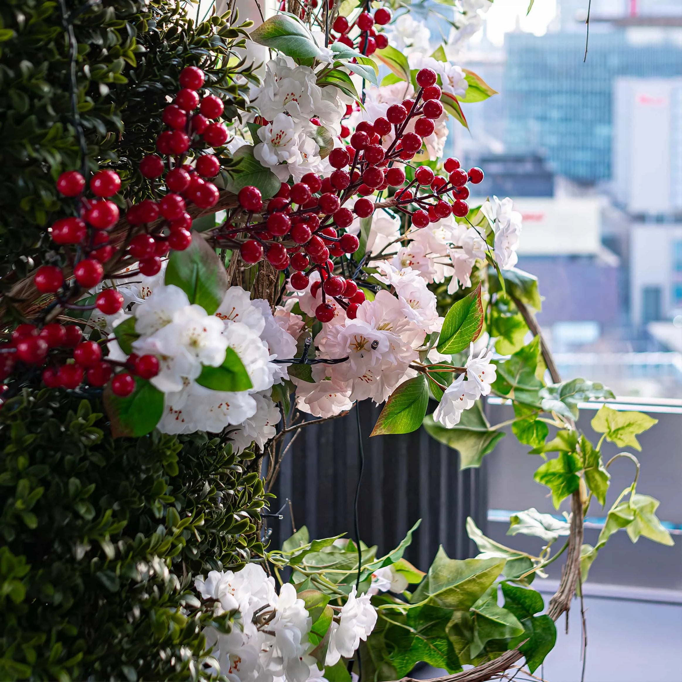 Vivid close-up of floral decoration with clusters of red berries and white flowers entwined with lush green leaves, set against an urban backdrop visible from the rooftop of STK Steakhouse.