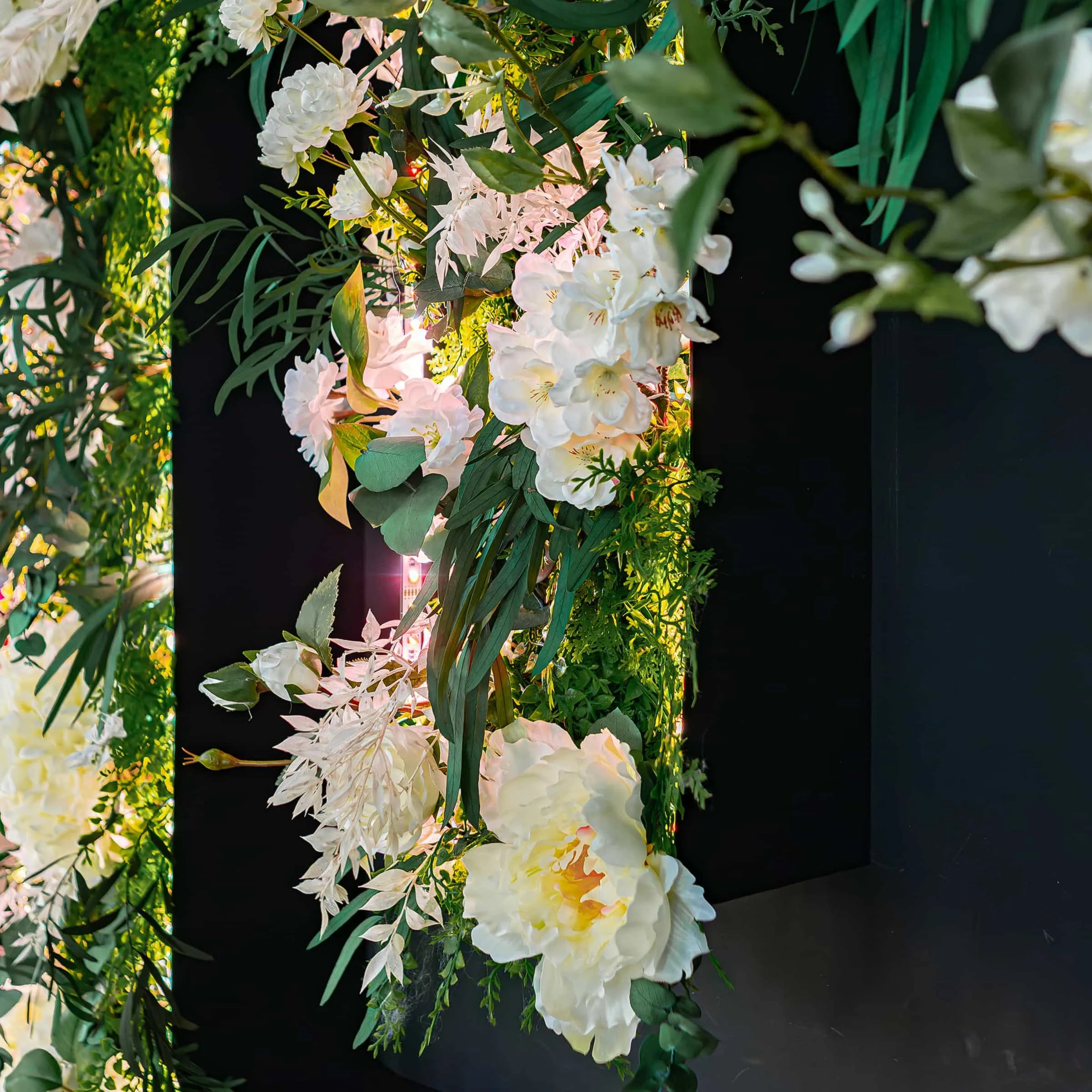 Side view of a lush floral wall at STK Steakhouse, with a cascade of white flowers, various green leaves, and subtle fairy lights creating a romantic and inviting atmosphere.