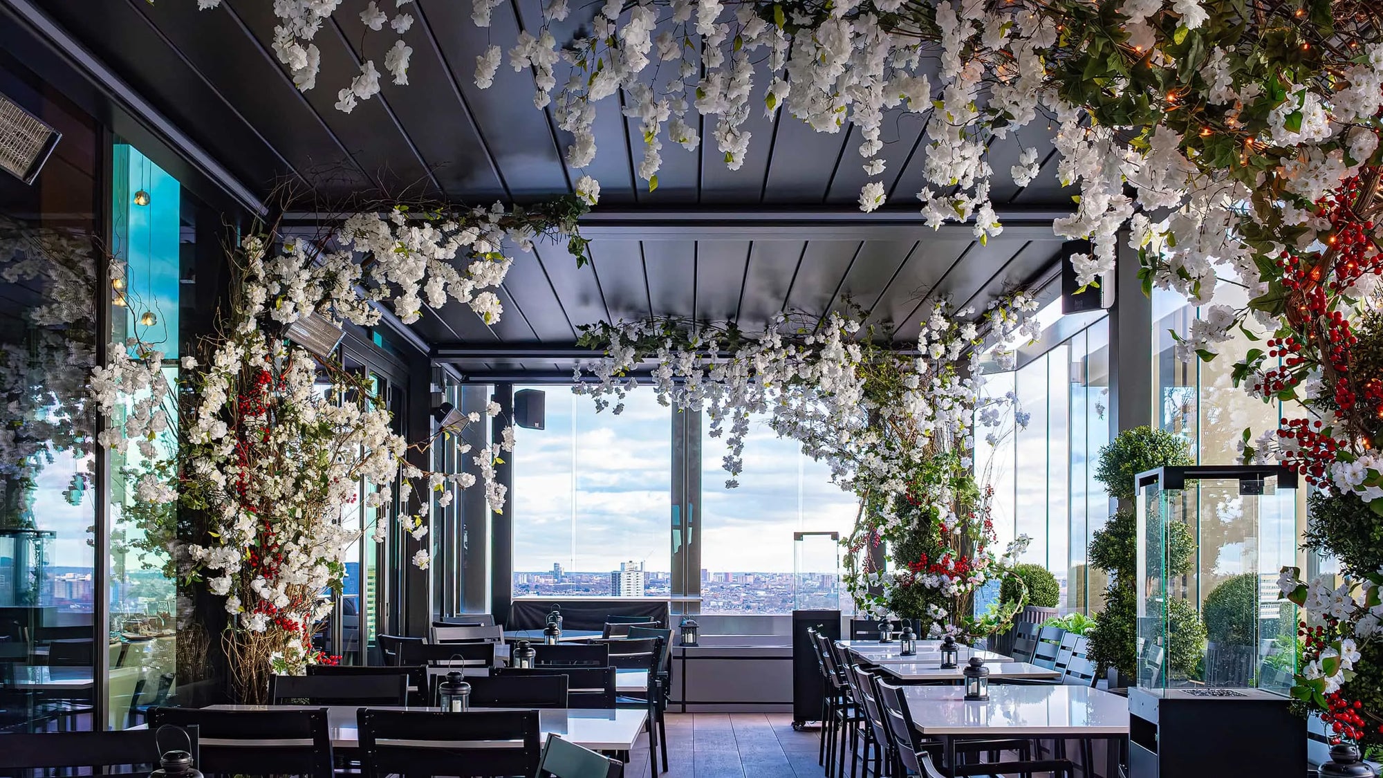 A view of the dining area at The STK Steakhouse in London decorated by Amaranté London's Christmas Floral Arrangements, with ceiling and pillars adorned with white blossoms and greenery, accented with red berries.