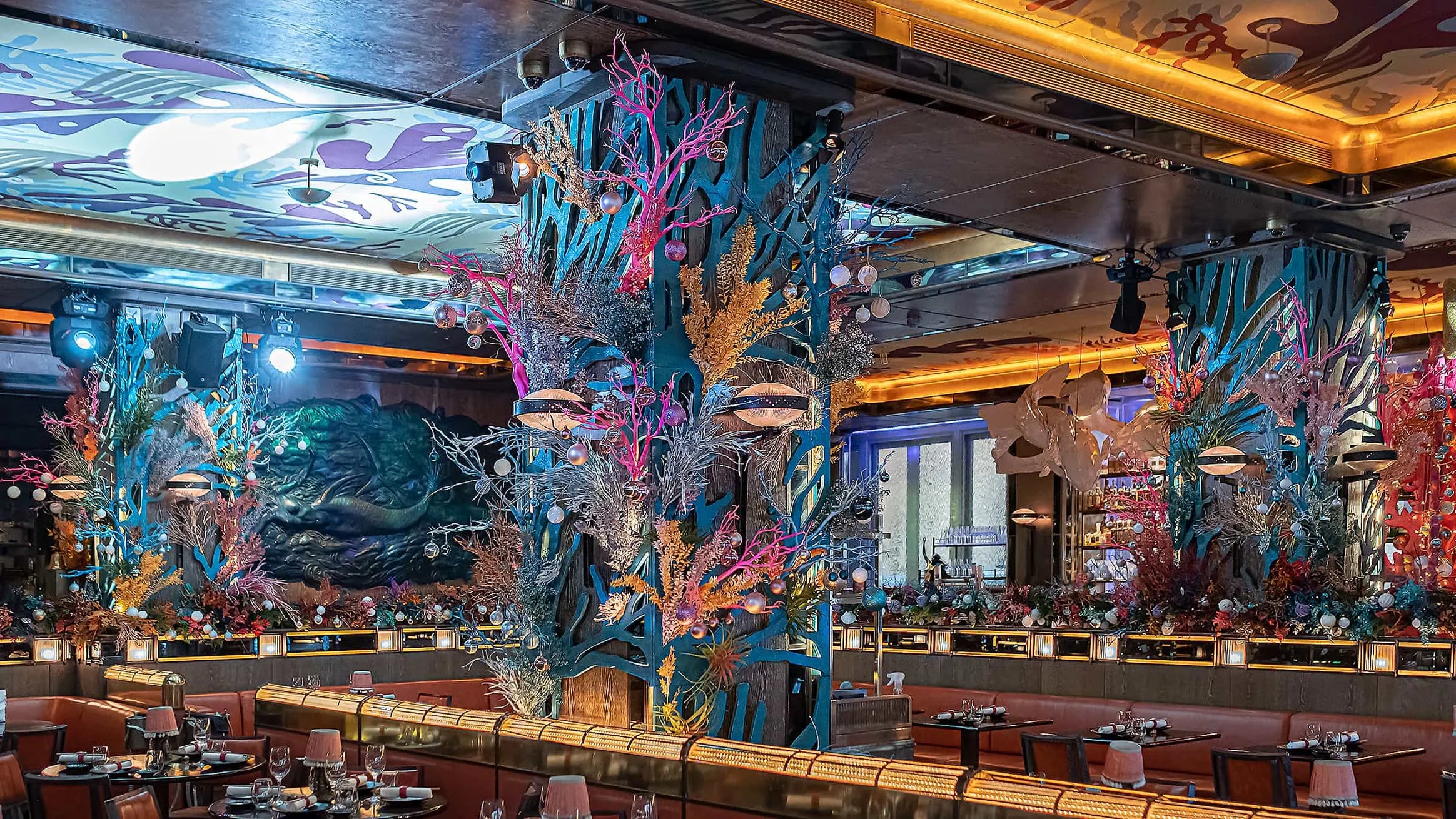 A stunning interior floral arrangement for Christmas by Amaranté London at Sexy Fish Restaurant features a mix of vibrant pink, blue, and white dried flowers enhanced with festive baubles.