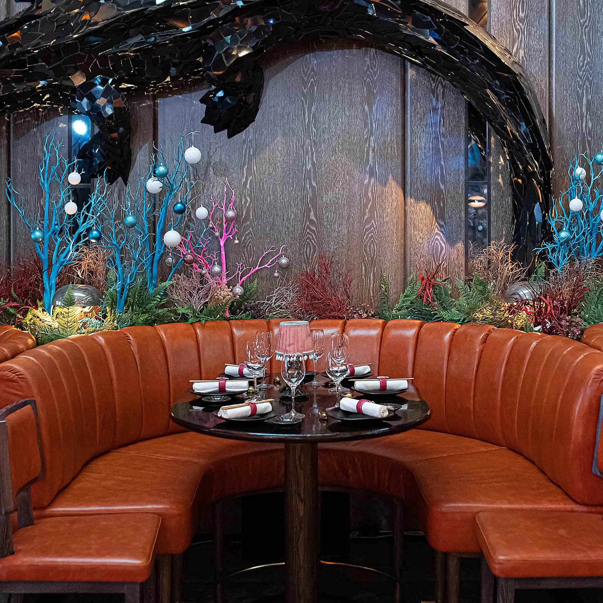 Luxurious dining area at Sexy Fish Restaurant, decorated by Event Florist Amaranté London with blue and pink coral-like stems, green ferns, and festive baubles, creating an elegant and festive Christmas atmosphere.