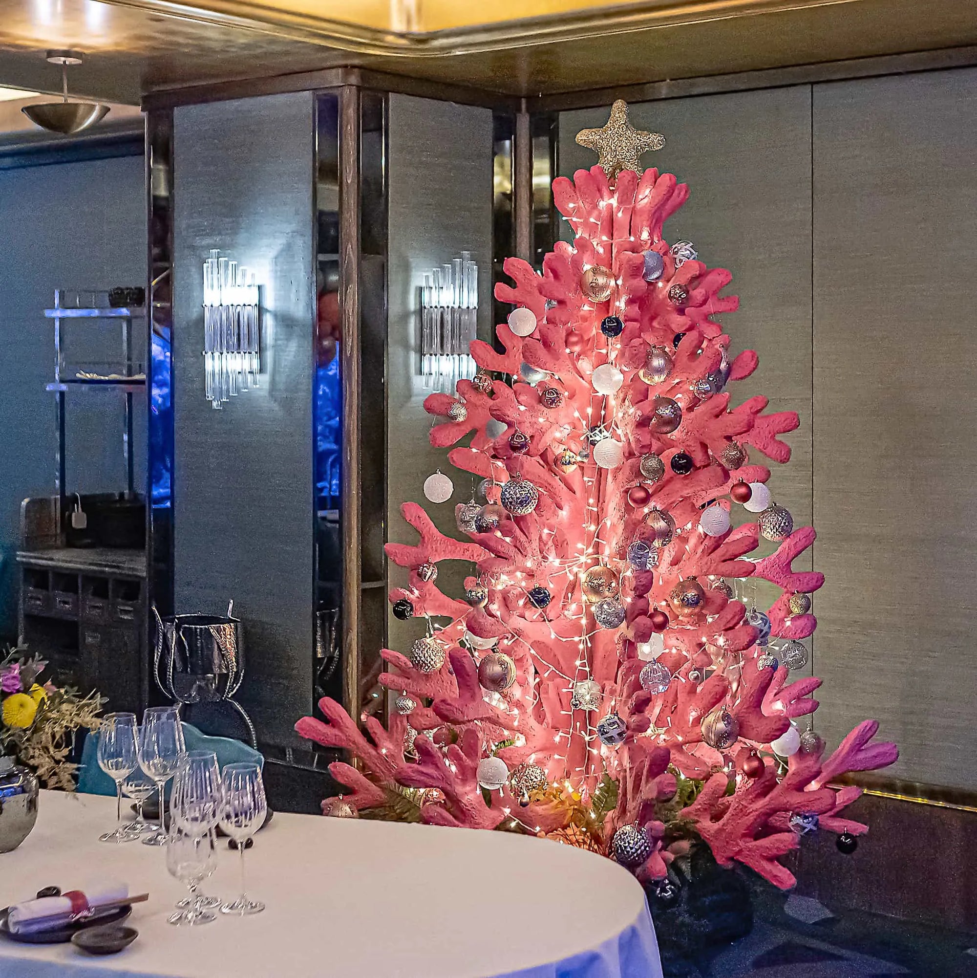 Coral-themed Christmas tree designed by Event Florist Amaranté London for Sexy Fish Restaurant, decorated with pink coral branches, twinkling lights, and silver baubles, creating a unique and cheerful festive centrepiece.