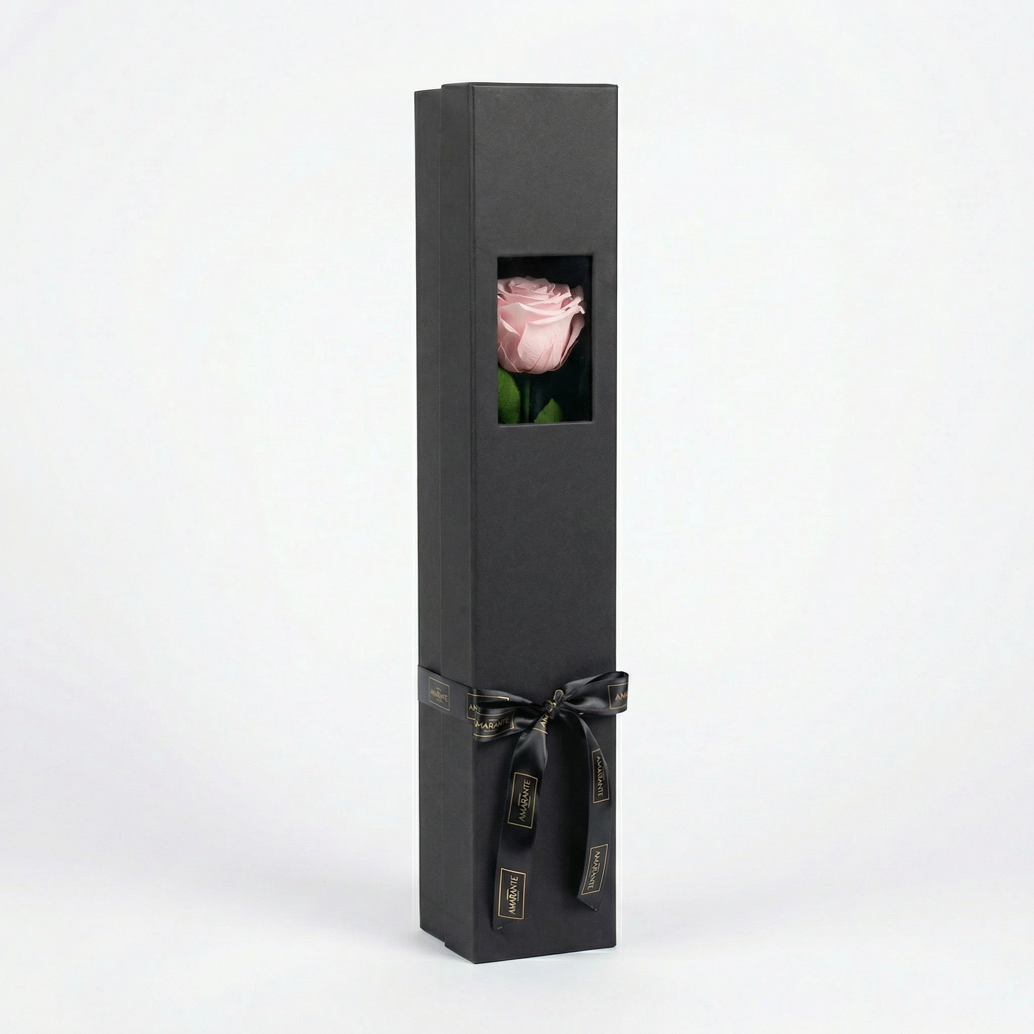 Sophisticated charcoal grey single rose presentation box featuring rectangular window showcasing delicate blush pink preserved rose with verdant stem, adorned with premium black ribbon - Amarante London