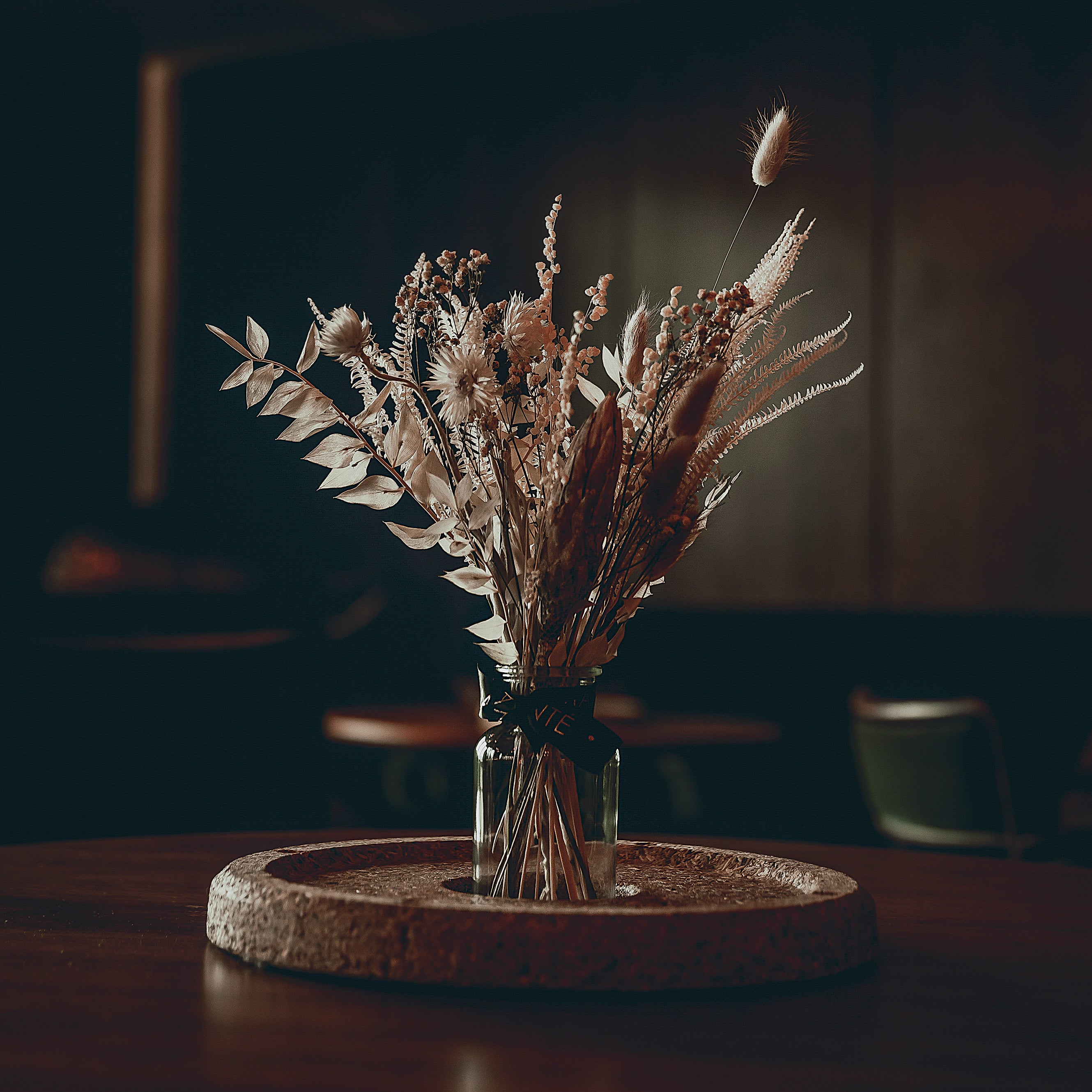 The grandeur of the White City House is enhanced by a striking event florist's creation by Amaranté, with silvery foliage and plumes rising from a clear vase on a cork centrepiece against the blurred backdrop of a plush lounge with hanging lights.