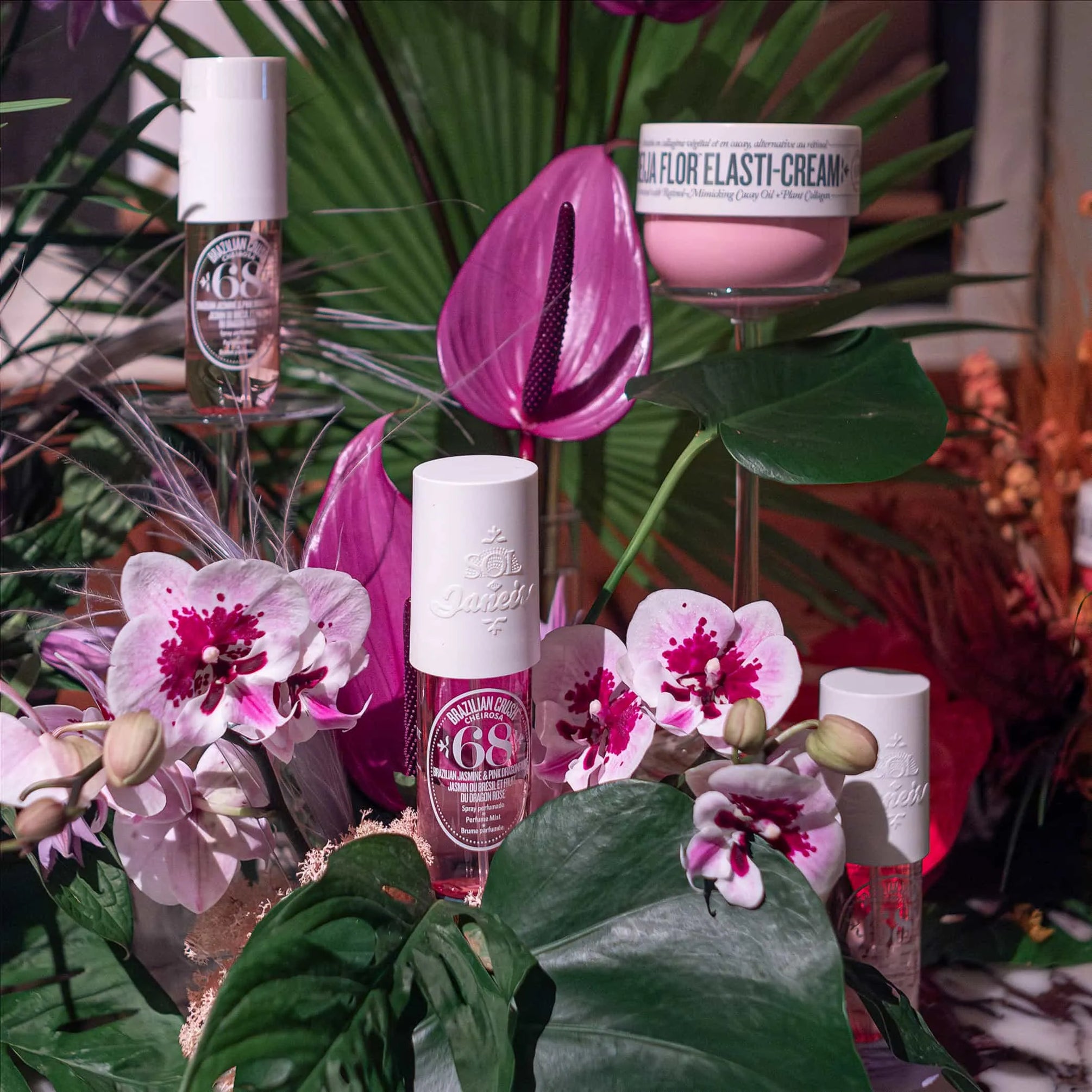Elegant floral display by Amaranté London featuring Sol de Janeiro skincare products, including the pink Beija Flor Elasti-Cream, surrounded by orchids and tropical foliage.