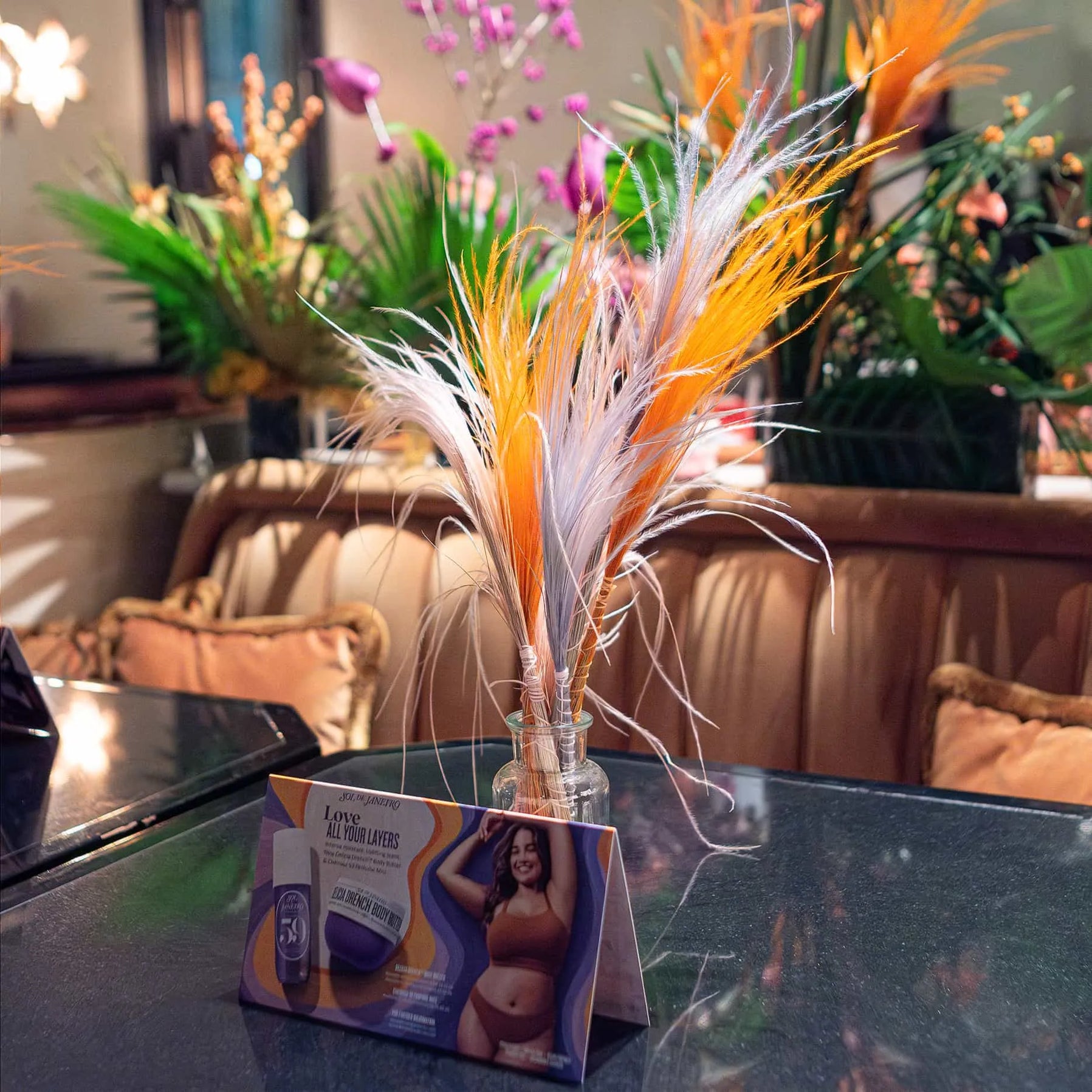 Sol de Janeiro promotional material displayed alongside a vibrant feather arrangement by Amaranté London in the sophisticated setting of Maine Mayfair restaurant.
