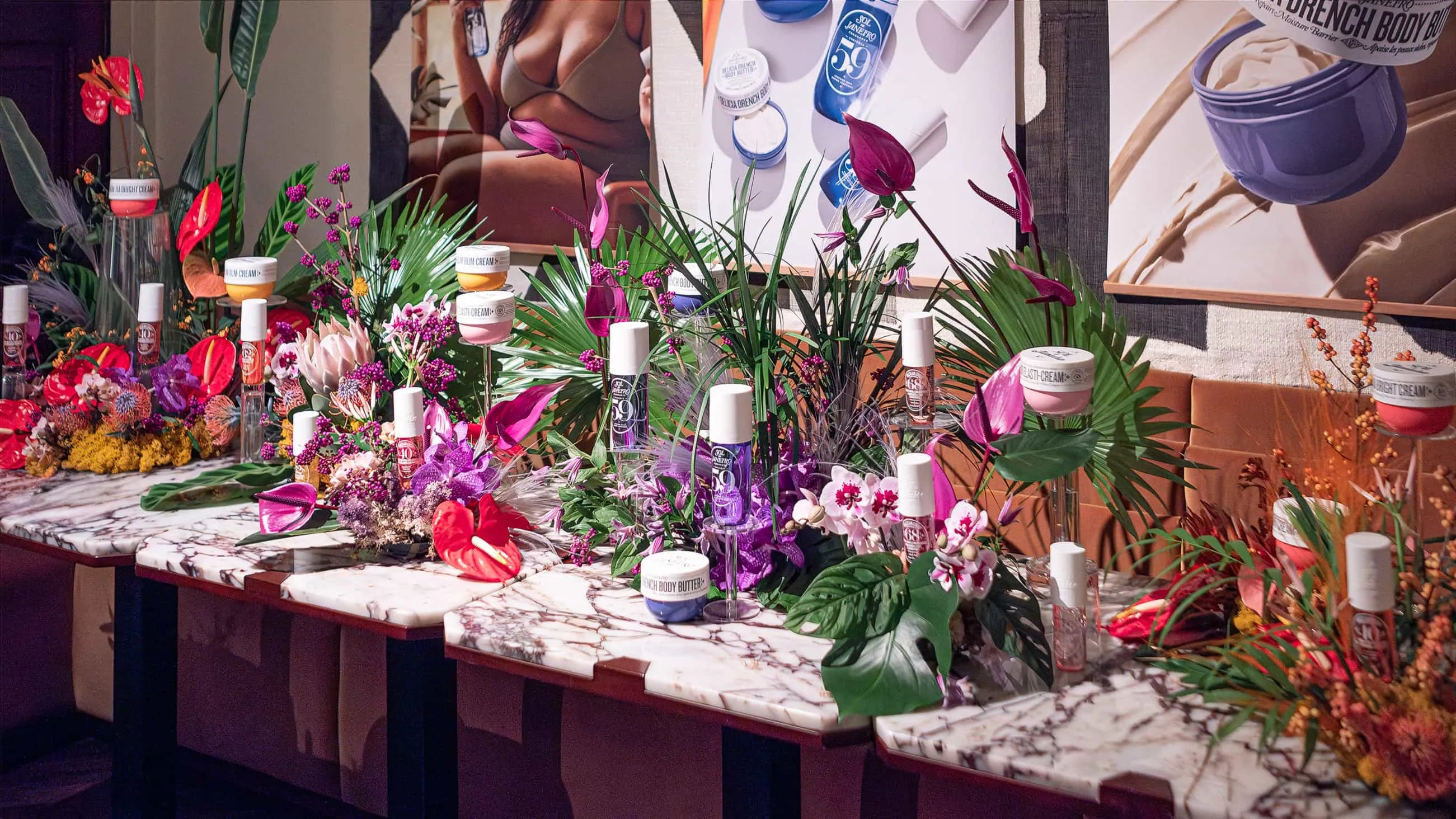 Vibrant bespoke floral installation by Amaranté London at Maine Mayfair restaurant featuring Sol de Janeiro products amidst exotic flowers and lush greenery on a marble countertop.