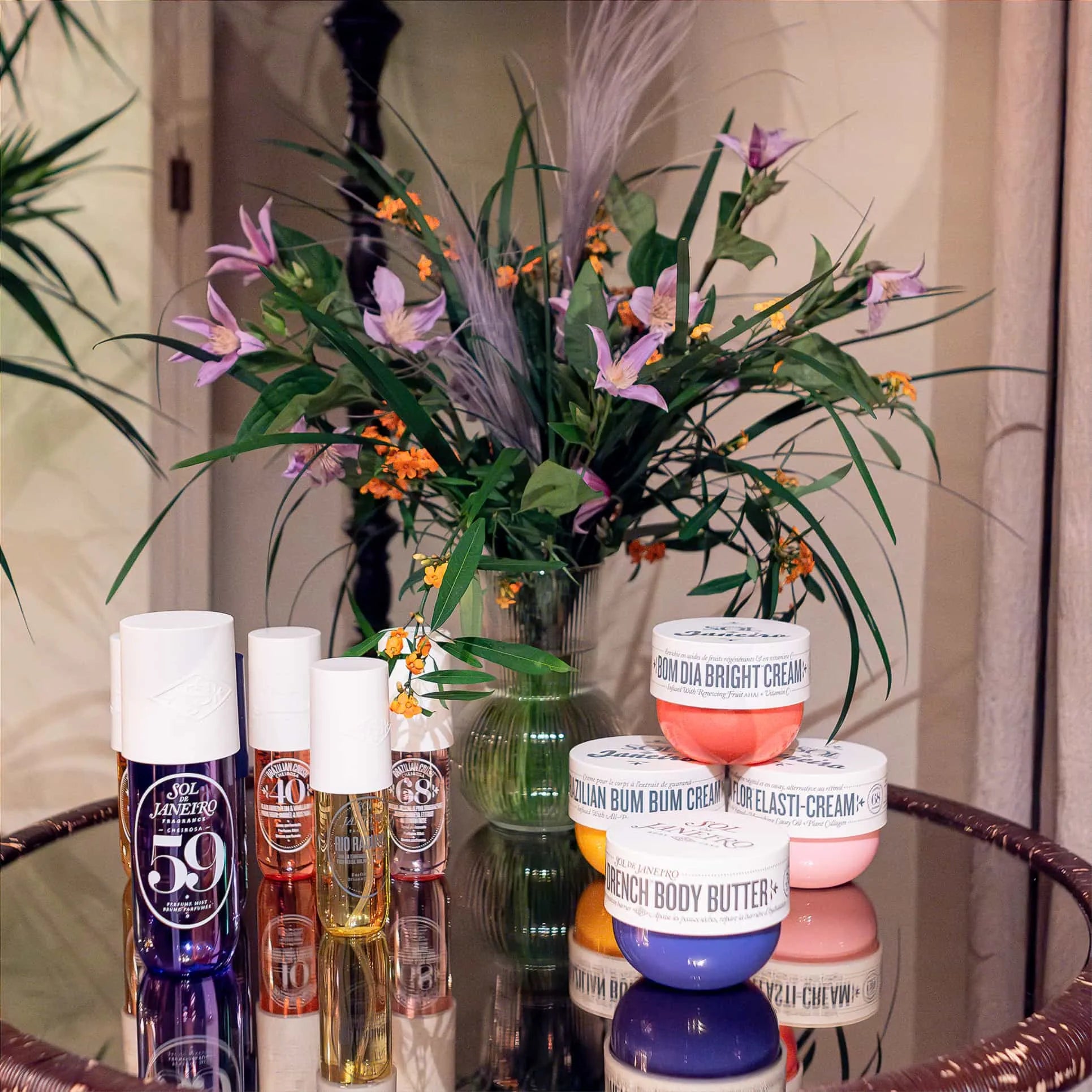 Sol de Janeiro skincare collection including Bom Dia Bright Cream and Brazilian Bum Bum Cream displayed on a glass table with Amaranté London's floral arrangement in the background.