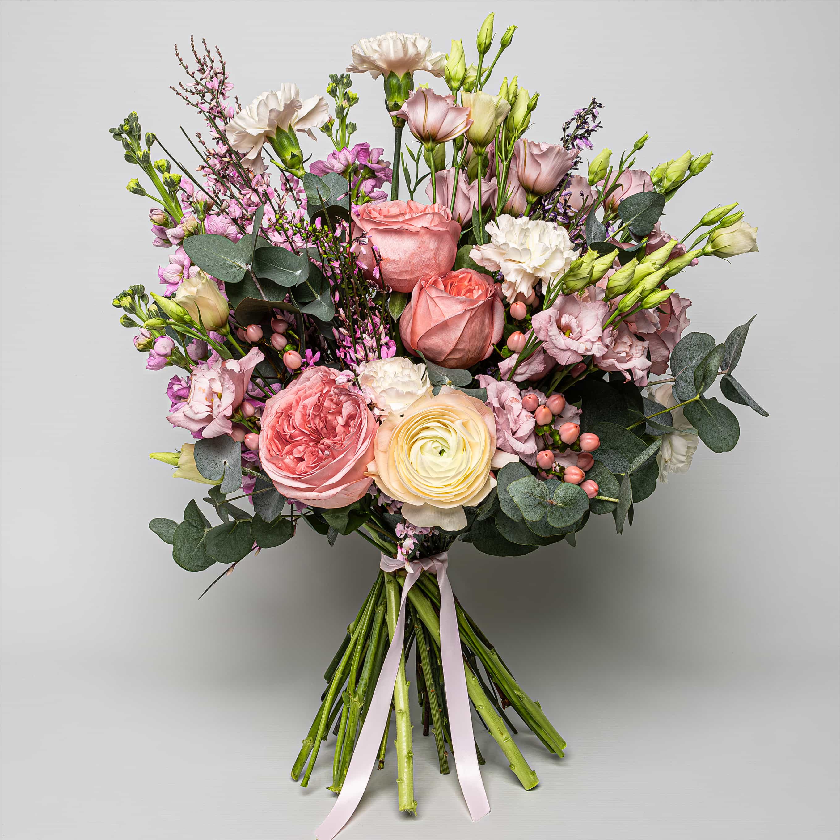 Spring Bloom Fresh Flower Bouquet is a luxury floral arrangement with several large, ruffled roses in varying shades of pink and peach, their opulent petals unfurling amidst the surrounding greenery. A delicate collection of blooms in soft pastel shades, suggesting sophistication and grace. It includes blushing pink roses, creamy white lisianthus, and hints of lavender and pale green, creating a harmonious visual symphony.