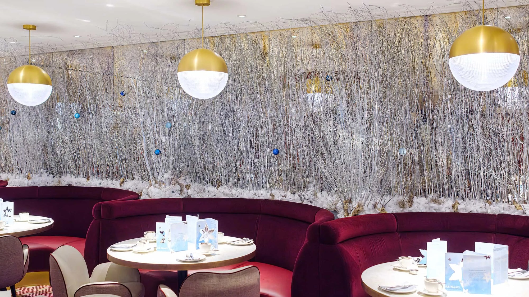 The dining area of the Strand Palace Hotel in London is decorated with a bespoke Christmas floral wall by Amaranté London. The wall uses white birch branches adorned with blue and silver baubles, creating an elegant wintery backdrop for the festive season.