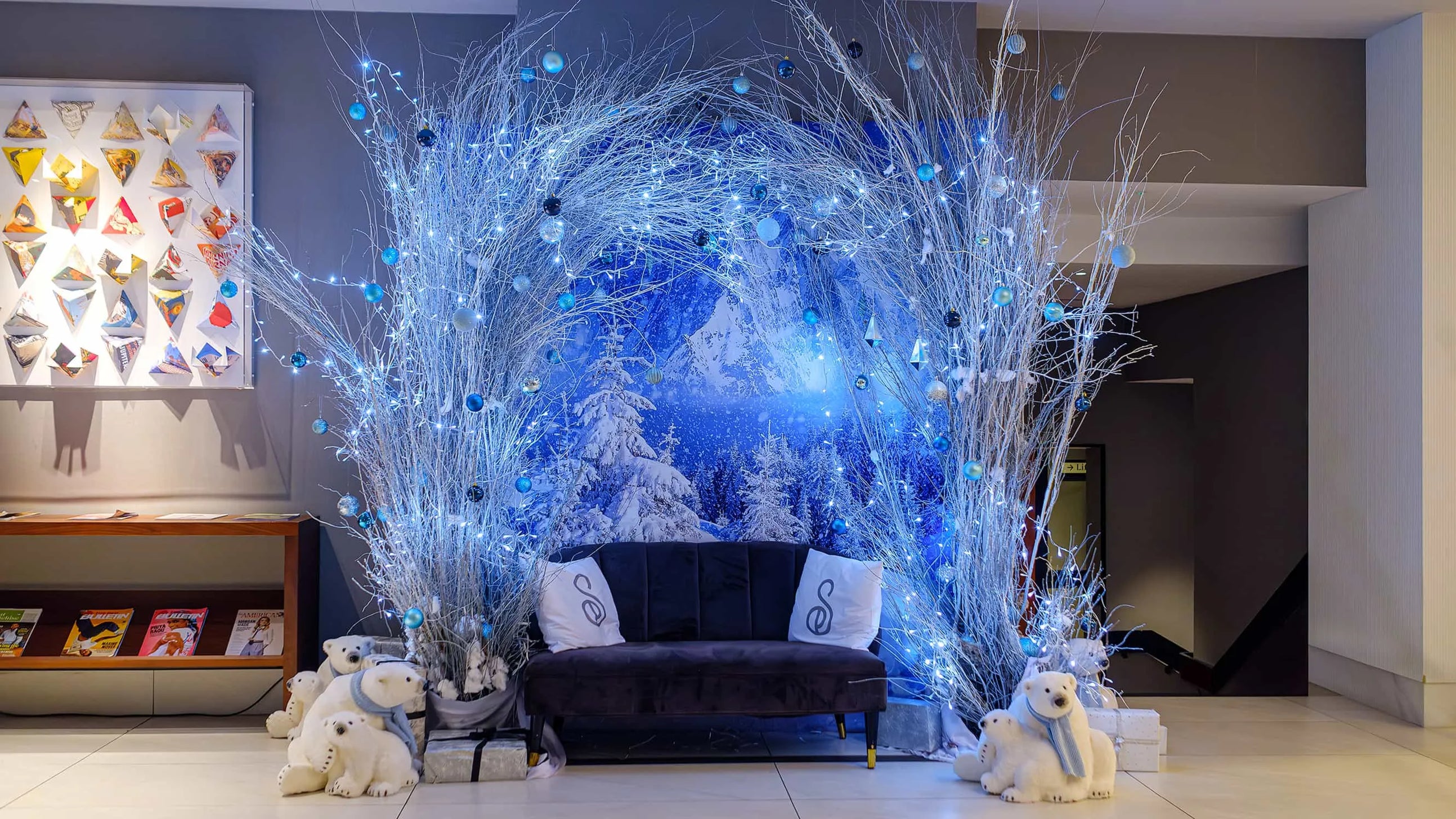 A beautifully lit floral arch installation at the Strand Palace Hotel in London, created by Event Florist Amaranté London for Christmas. The arch features white birch branches and blue baubles, complemented by a winter wonderland backdrop, perfect for festive photos.