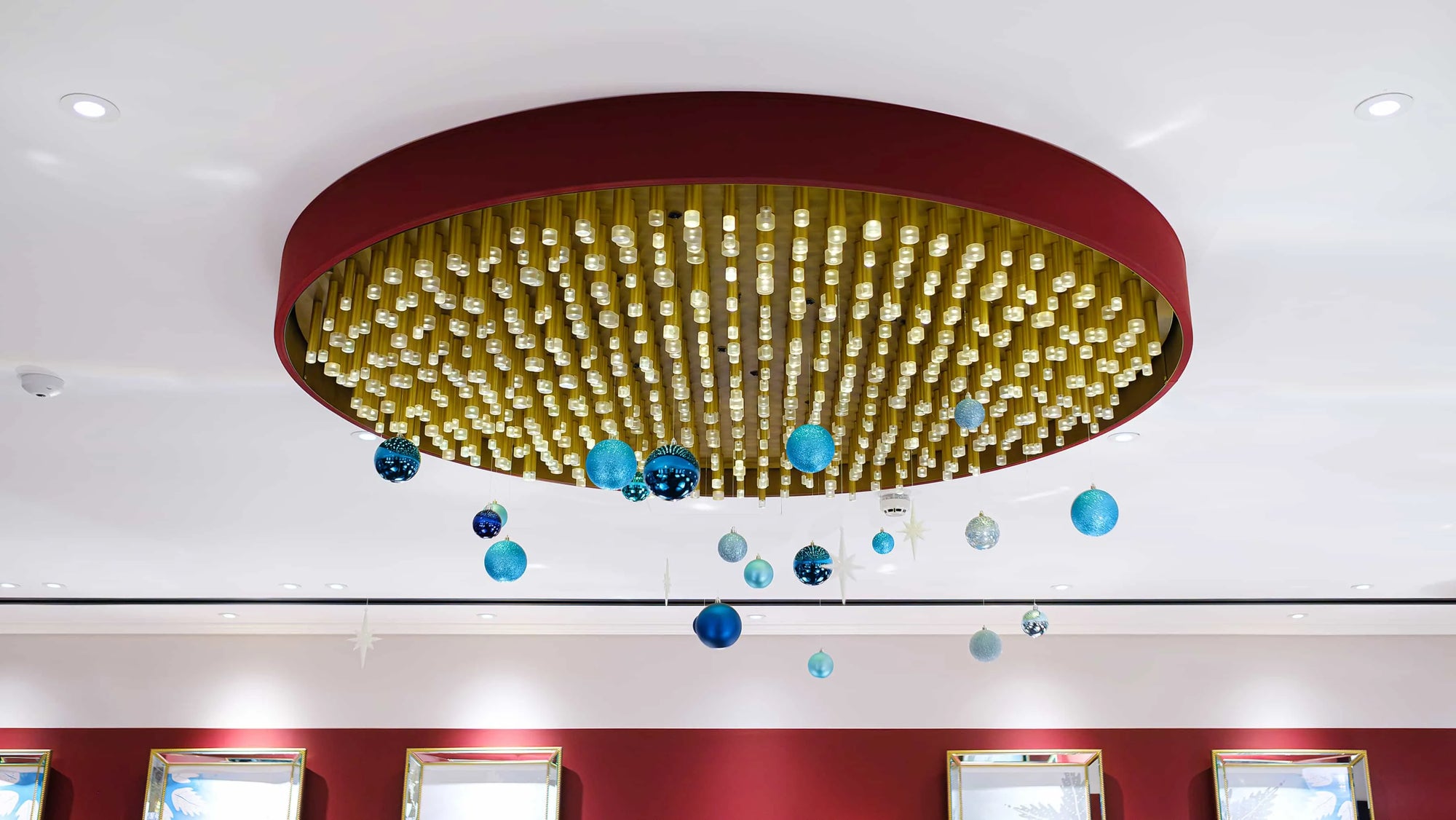 A sophisticated hanging floral arrangement at the Strand Palace Hotel in London featuring blue and silver baubles suspended from a golden chandelier adds a touch of festive elegance to the space. Designed by event florists Amaranté London.