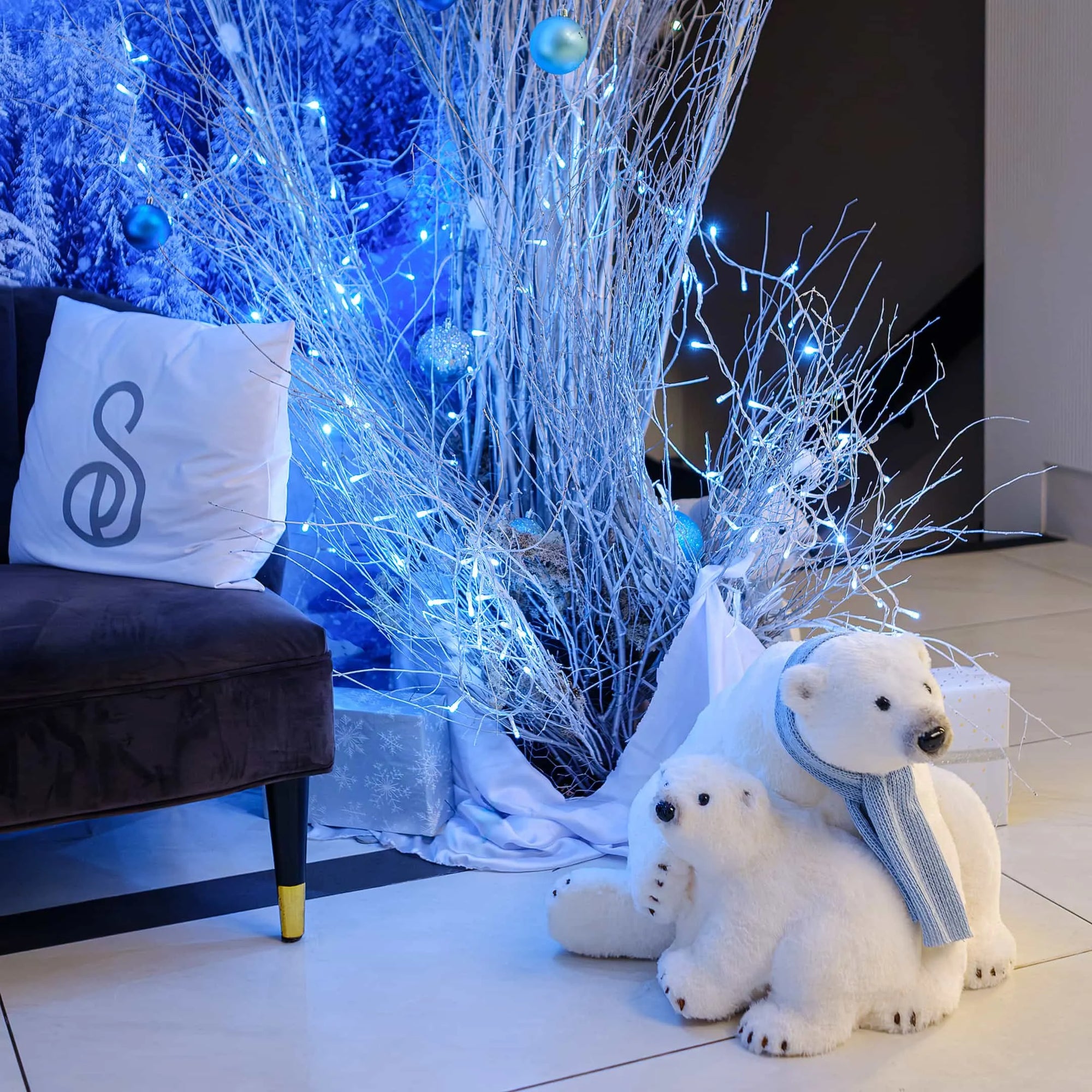 A cosy seating area at the Strand Palace Hotel in London, decorated with a Christmas floral installation by Amaranté London. The setup includes white birch branches with blue lights, plush polar bear decorations, and a wintery backdrop, creating a cheerful festive ambience.