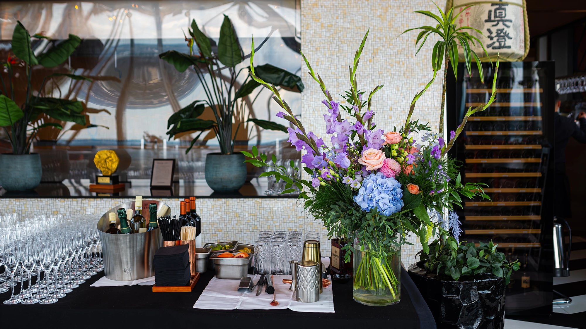 Seasonal bar arrangement featuring blue hydrangea, purple delphiniums and peach roses, created for Sushi Samba London by Amarante London