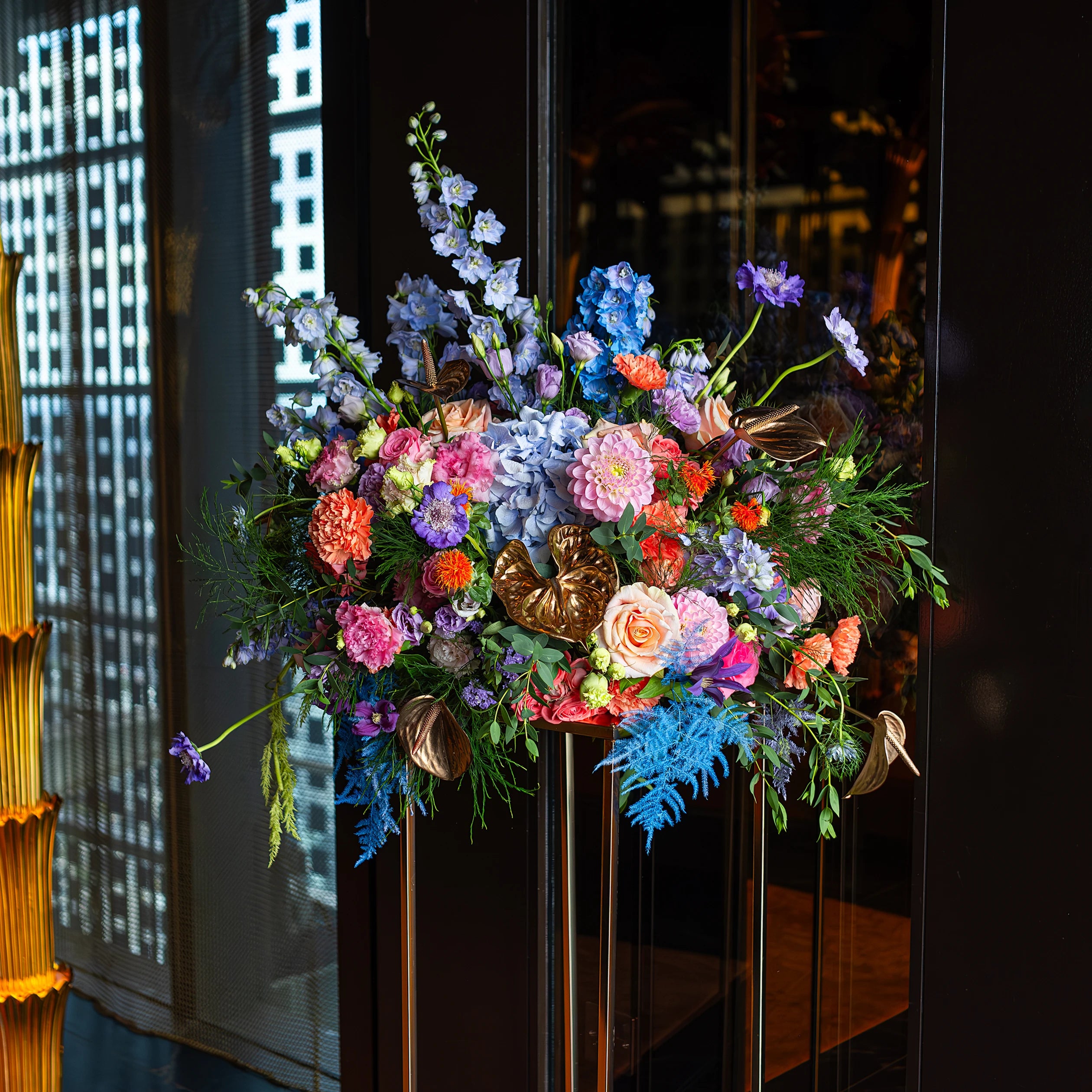 A luxurious floral arrangement featuring blue hydrangeas, peach roses, and lush green foliage is placed on a dining table to add elegance and vibrancy to the birthdy celebration atmosphere.