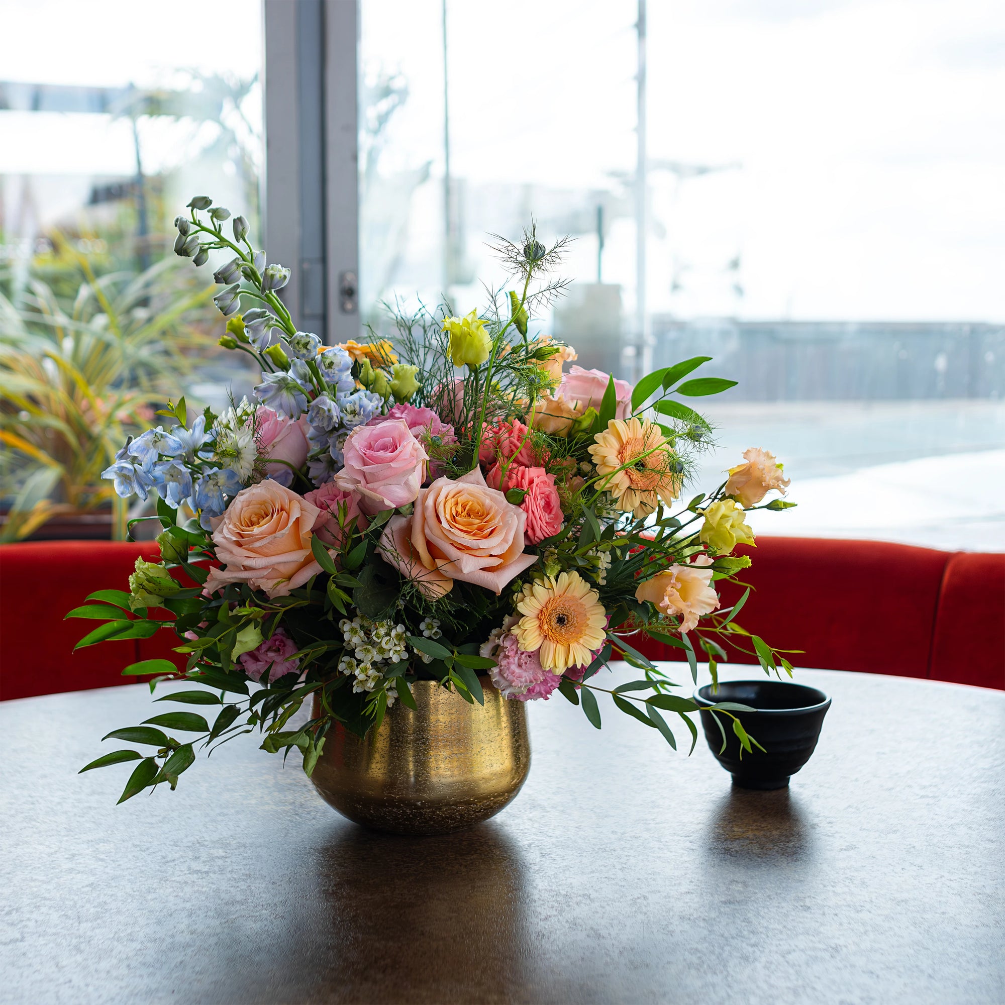 An elegant table flower arrangement featuring pink roses, peach carnations, and lush green foliage in a golden vase enhances the table setting with a touch of luxury - Amaranté London