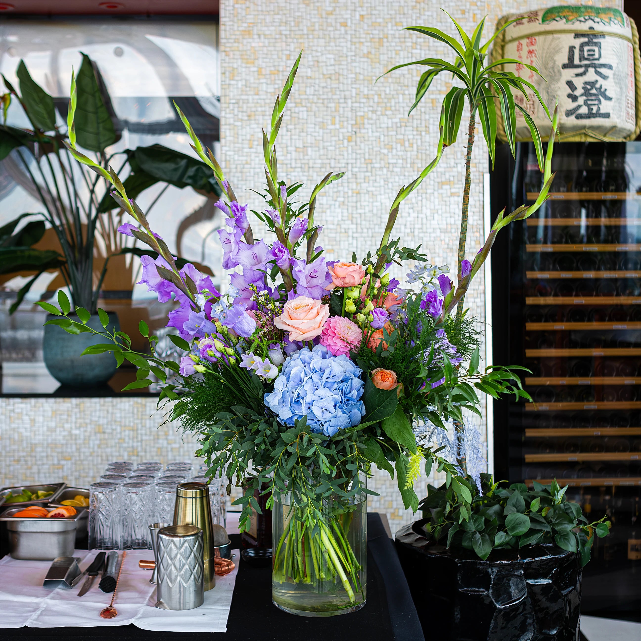 A beautifully arranged floral centrepiece for a birthday event at Sushi Samba, featuring a mix of pink roses, peach carnations, and blue hydrangeas, creating a luxurious and inviting atmosphere on the table - Amaranté London