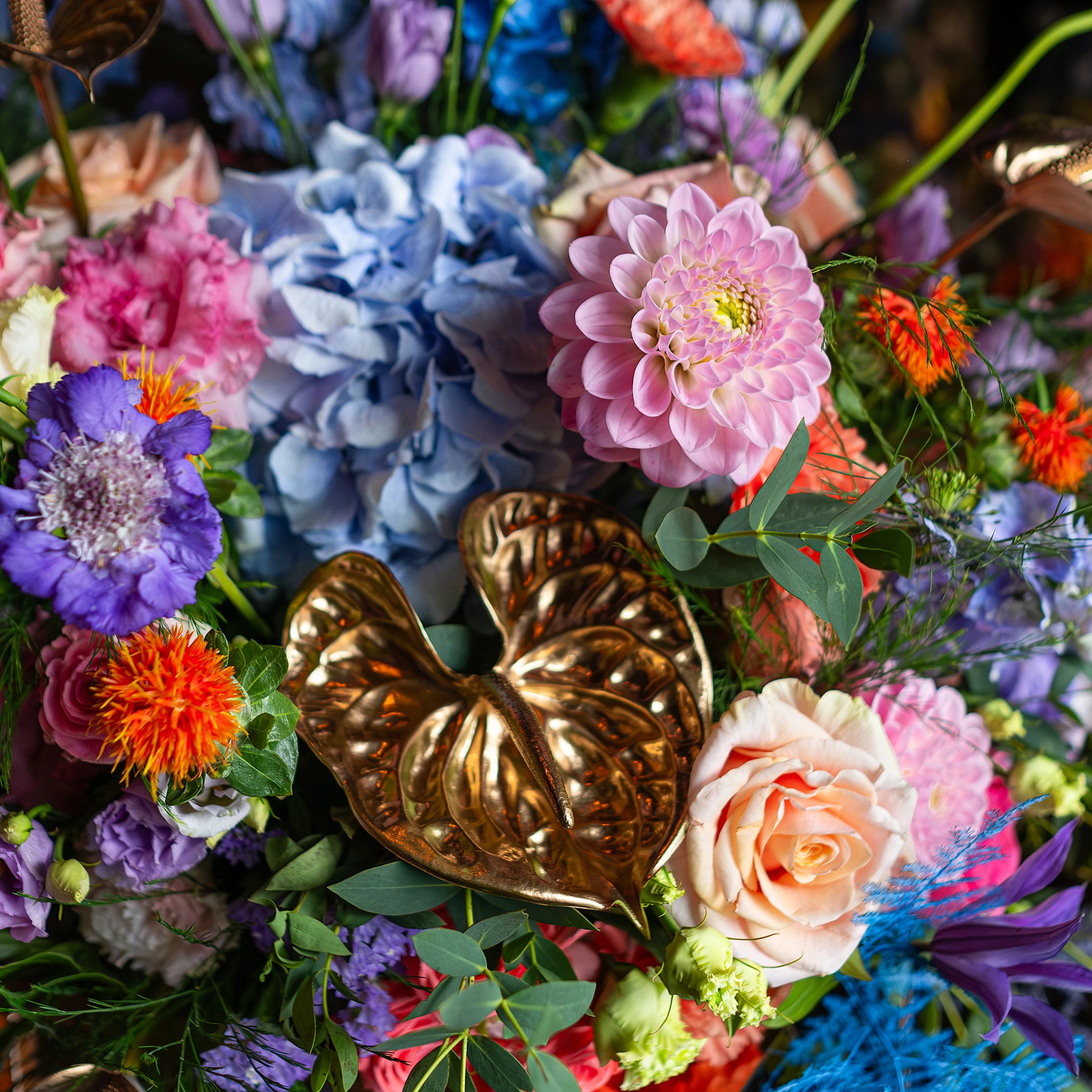 Close-up of a vibrant floral party decoration for a birthday event at Sushi Samba, featuring pink dahlia, blue hydrangea, and golden anthurium leaves, capturing the luxurious and festive atmosphere of the venue with a mix of bright colours.