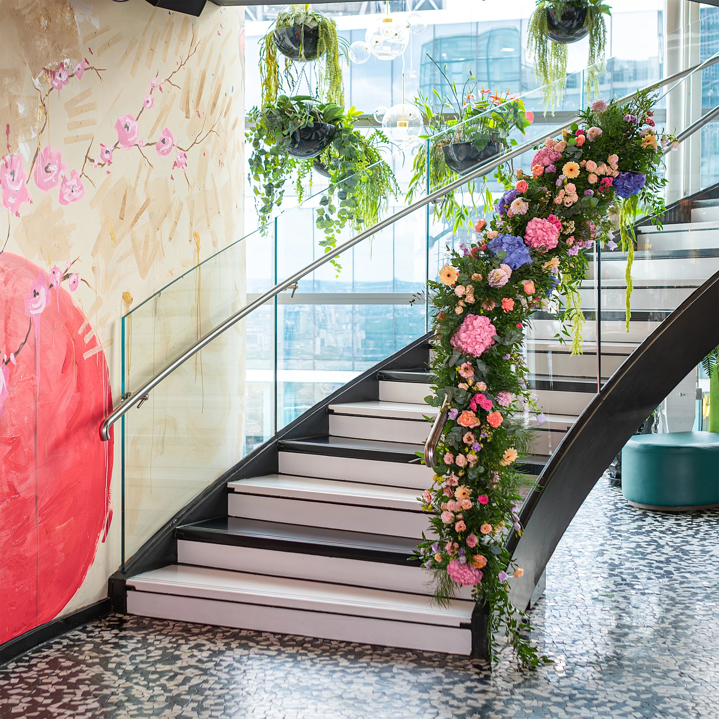 A grand staircase at Sushi Samba is adorned with a cascading floral party decoration for a birthday event, featuring pink hydrangeas, peach roses, and trailing greenery, adding a touch of elegance and sophistication to the venue - Amaranté London, Event Florist