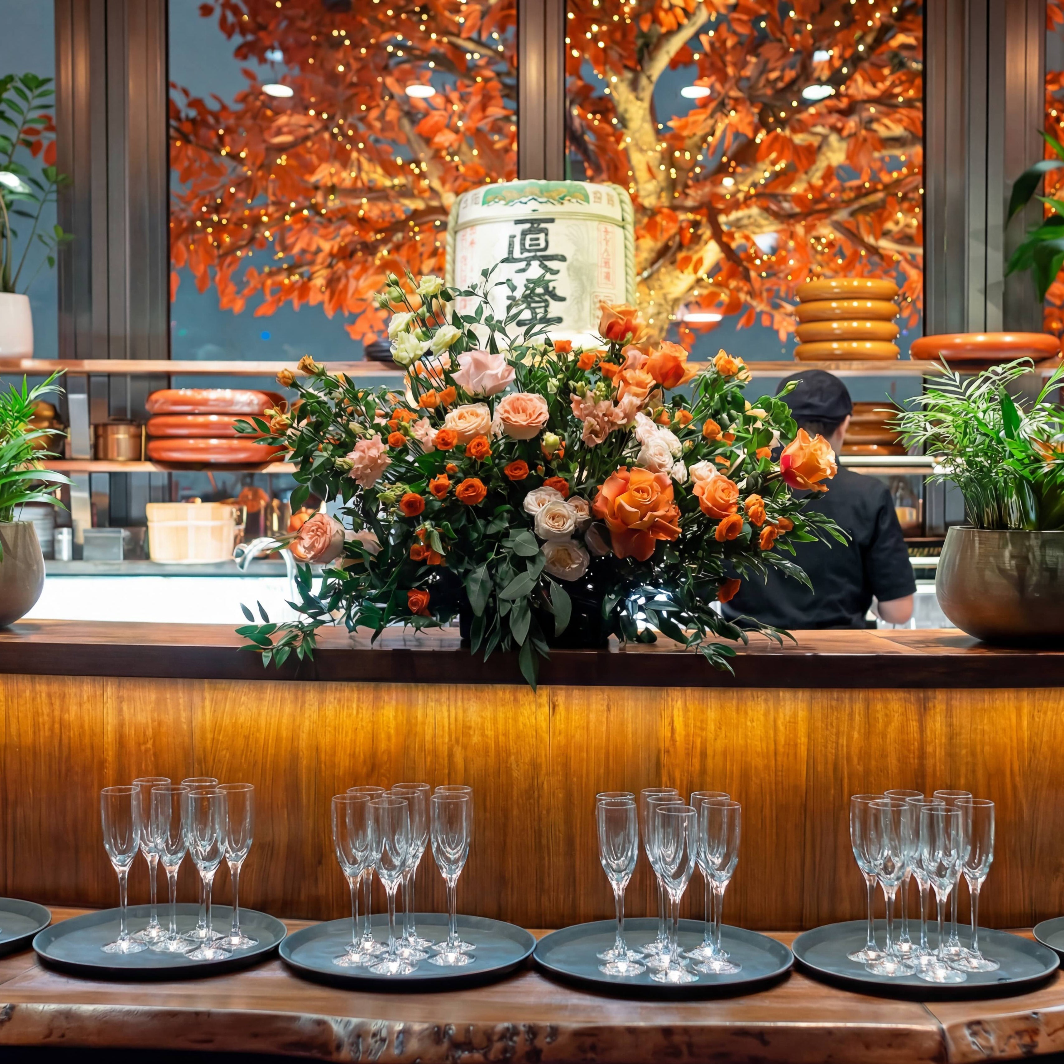 Low restaurant bar arrangement featuring orange and peach roses styled on the pass at Sushi Samba London by Amarante London