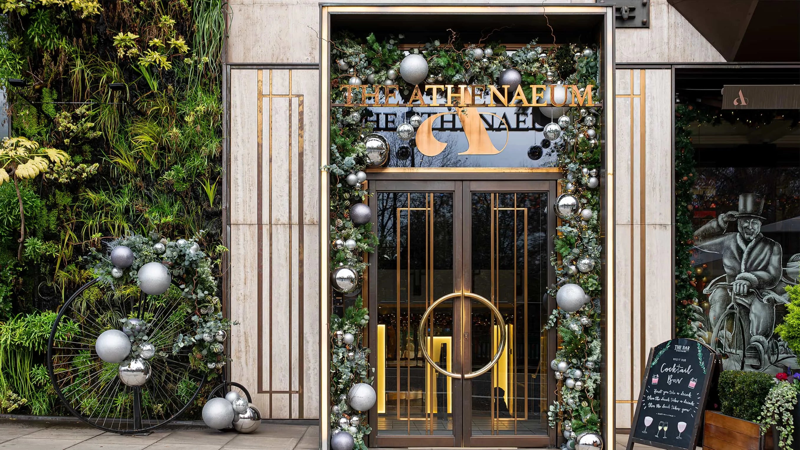 A grandiose Christmas floral arrangement for The Athenaeum in London by Amaranté London Event Florist, capturing the winter spirit with an opulent mix of festive greenery, twinkling lights, and elegant silver ornaments, perfectly framing the hotel's luxurious entrance.