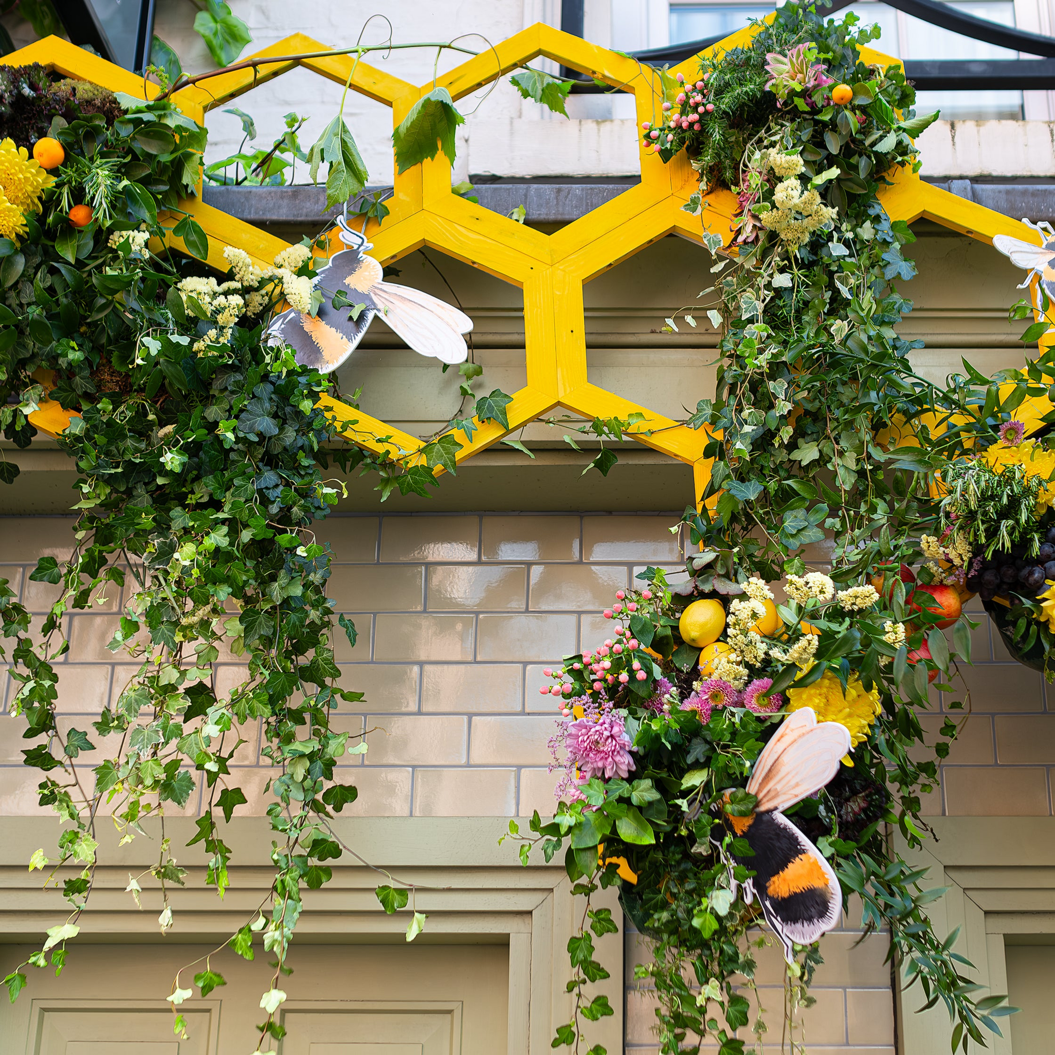 A close-up view of the bespoke flower arrangement designed, created, and installed by event florist Amaranté London for The Five Fields for Chelsea in Bloom. This floral arrangement features detailed honeycomb elements, vibrant foliage, and a rich tapestry of fruits and flowers highlighting sustainability and natural beauty.