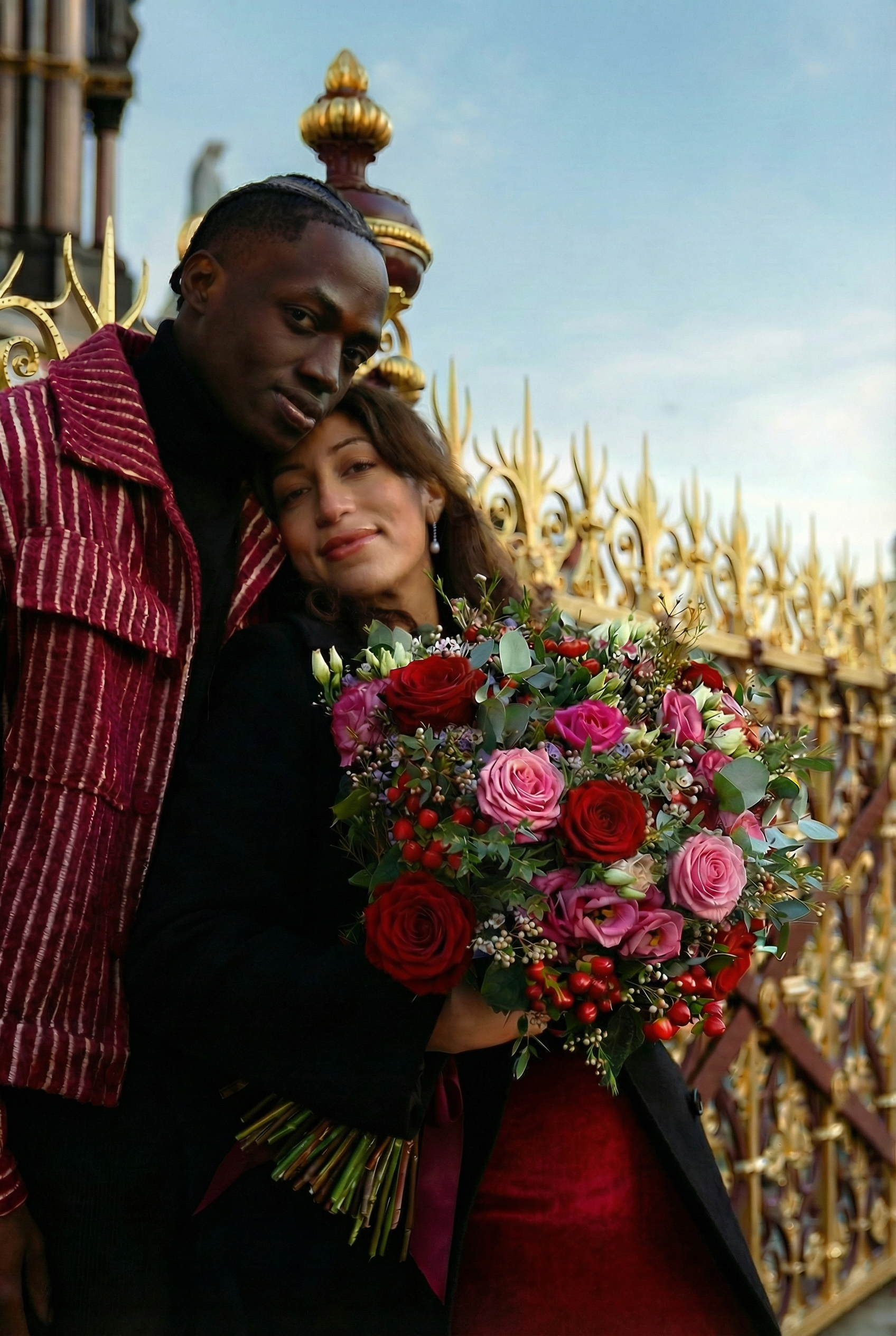 A man holding a large bouquet of 100 red roses with eucalyptus from Amarante London with his girlfriend approaching