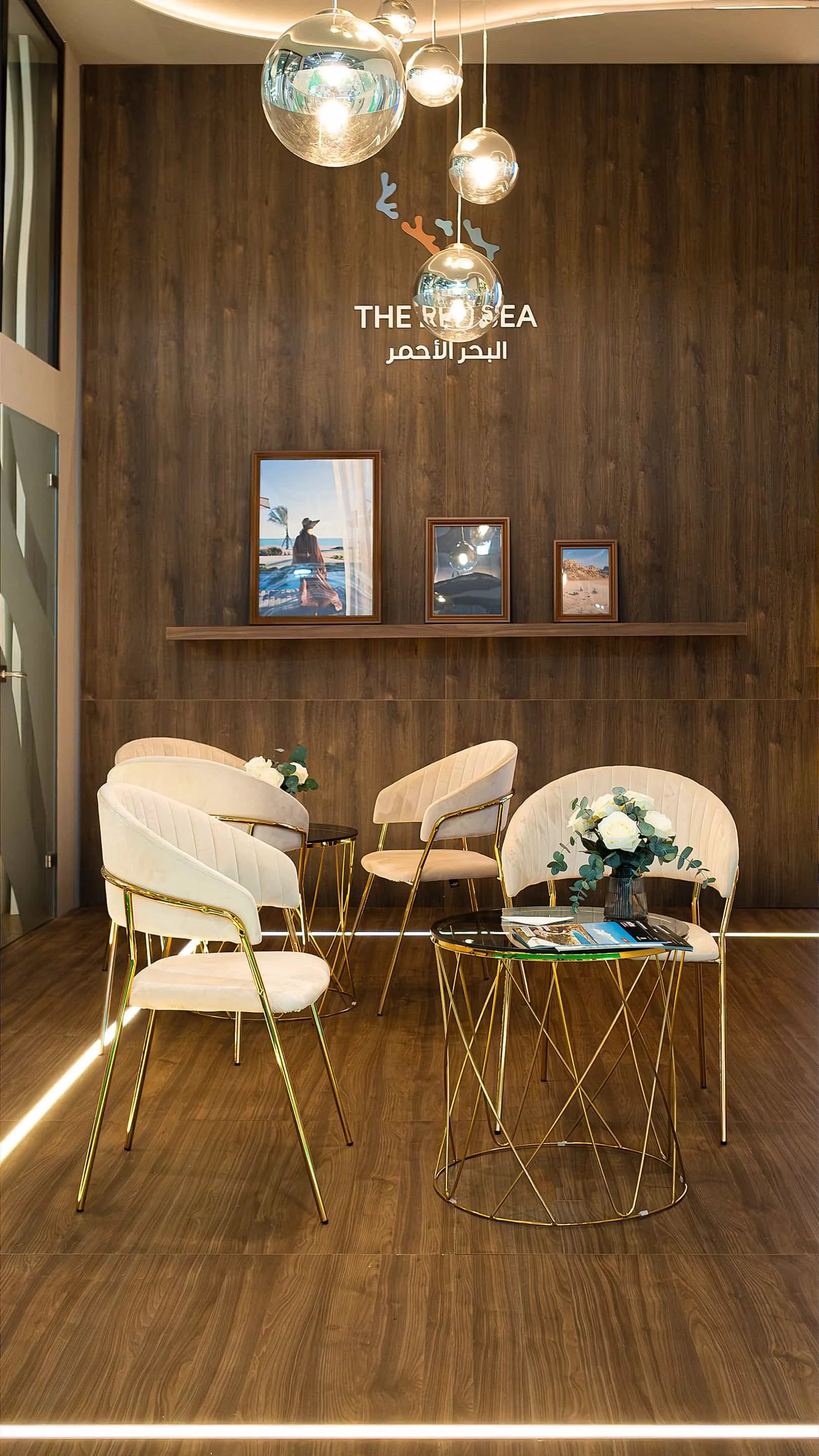 Chic lounge area at WTM, styled by Amaranté London with elegant white armchairs and gold accent tables, complemented by white floral arrangements featuring pure white roses.