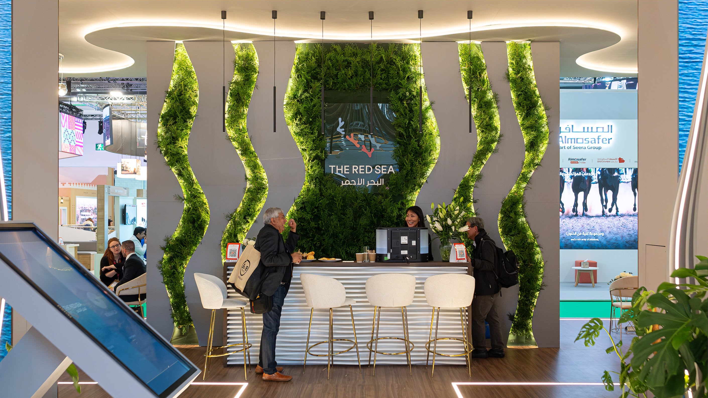 A Vibrant corporate event space at WTM London designed and created by Amaranté London. This bespoke floral arrangement features green foliage spirals, showcasing eco-friendly luxury for Red Sea Global.