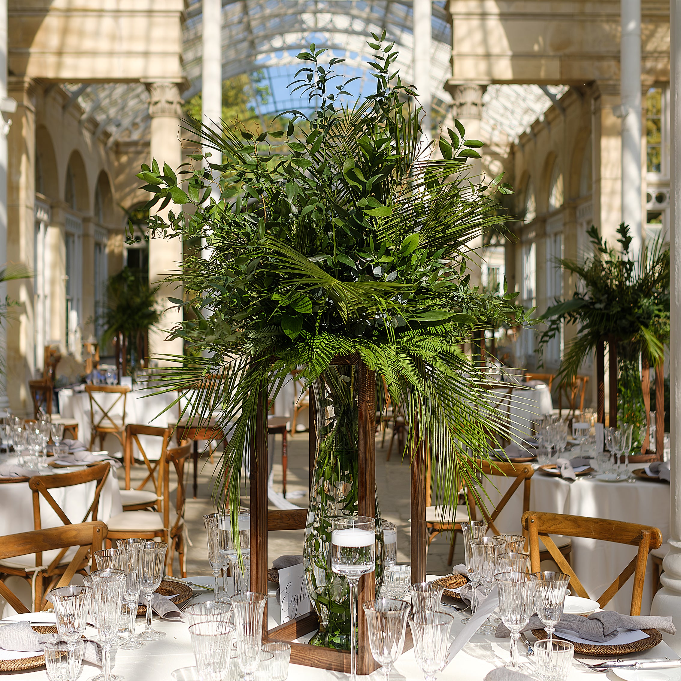 Tall tropical palm and fern centerpiece arrangement in glass vases, creating dramatic height on the conservatory dining table - Amaranté London