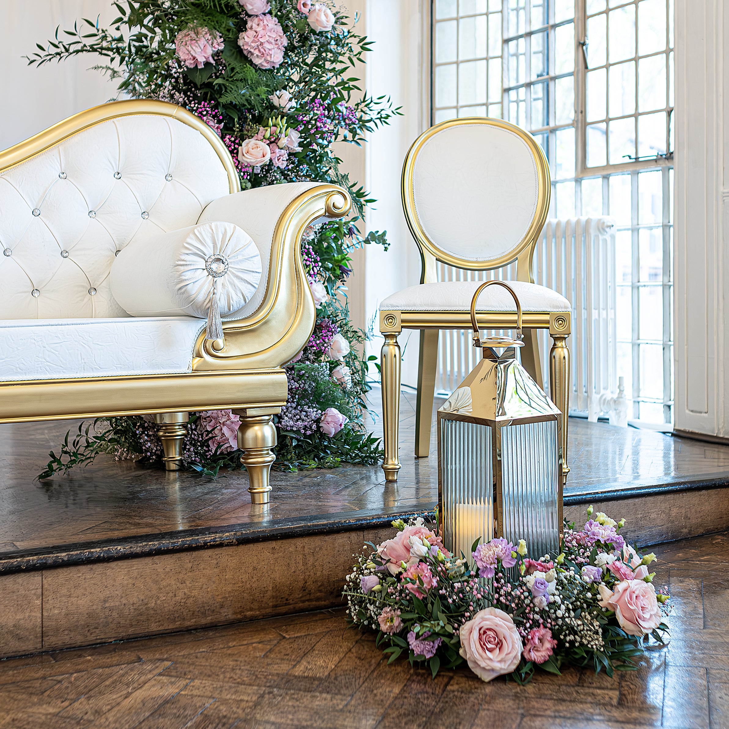 Intimate wedding floral vignette featuring pink roses and purple blooms arranged around a golden lantern beside ornate seating - Floral Design by Amaranté London, styling touches that enhance luxury wedding events