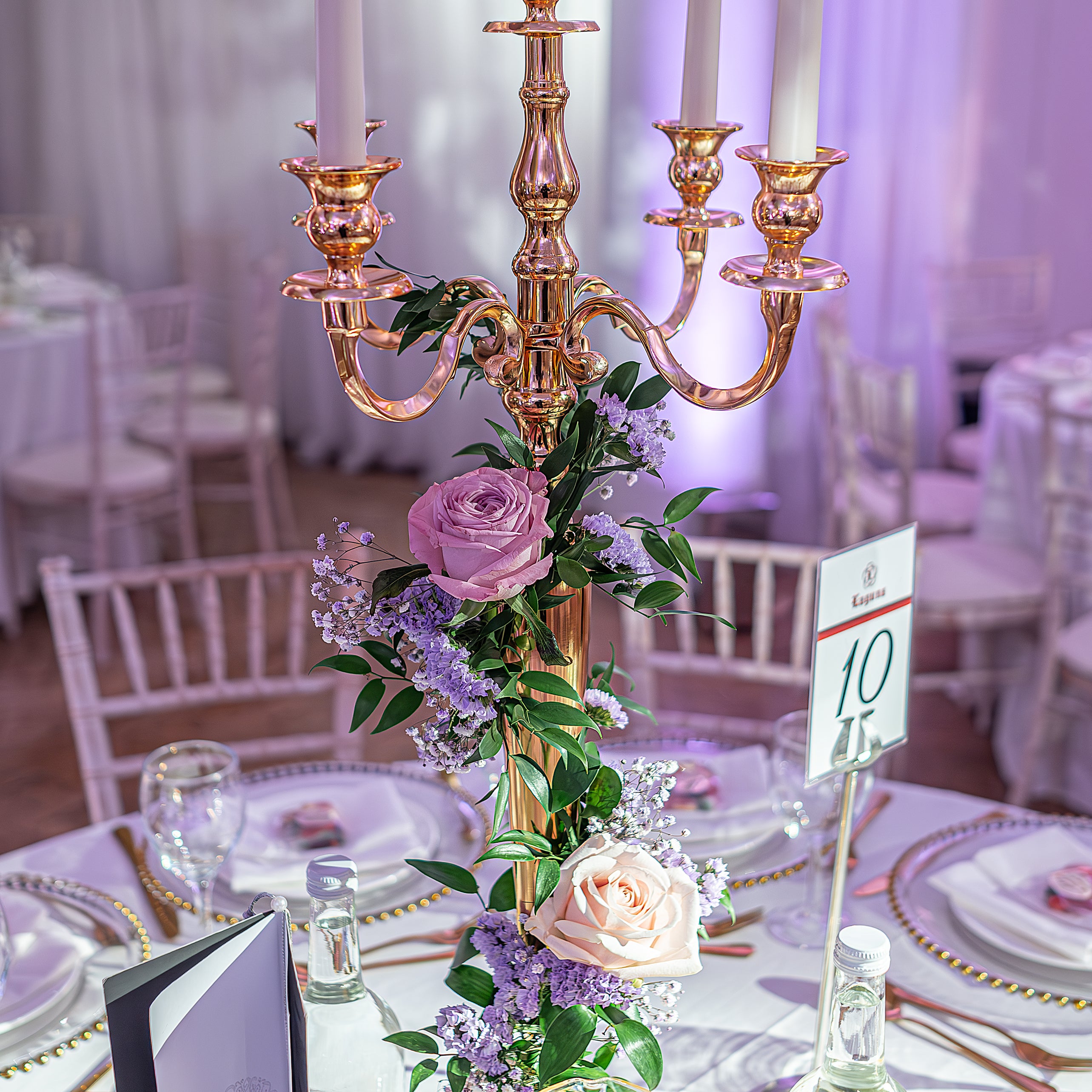  Elegant candelabra centerpiece adorned with purple and blush roses, plus delicate flowering sprigs on a formal dining table - Amaranté London