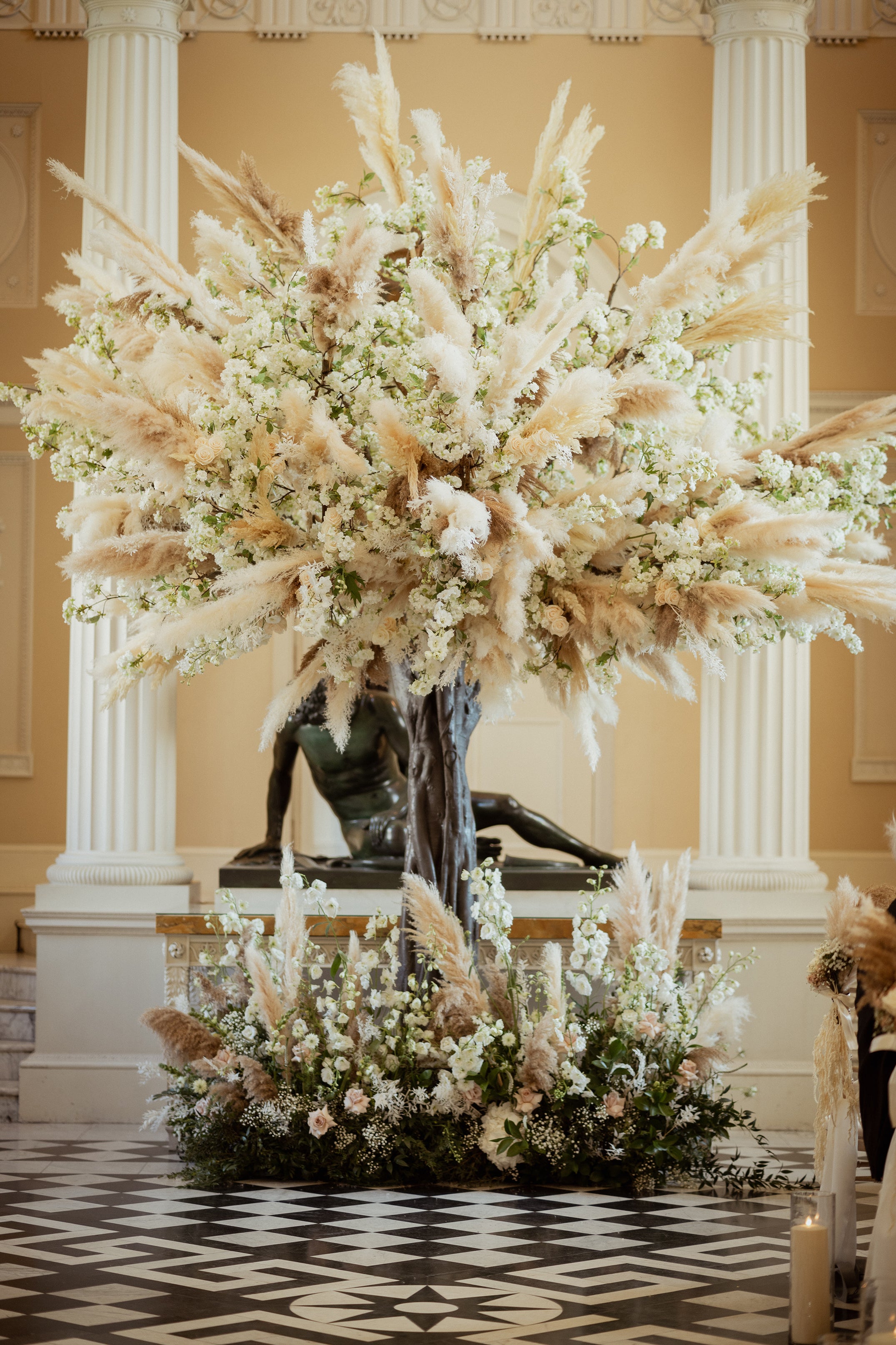 Close-up detail of a floral arrangement featuring abundant pampas grass and white blooms creating a sculptural display in a classical wedding venue - Amaranté London