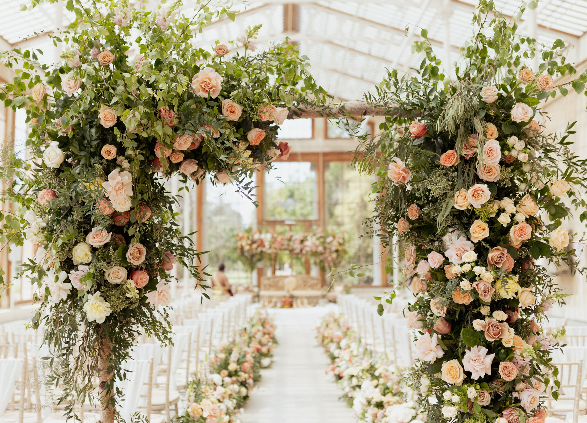 Elaborate floral ceremony archway featuring peach and cream roses with abundant greenery creating a natural canopy framework, large-scale wedding venue floral installations - Amaranté London