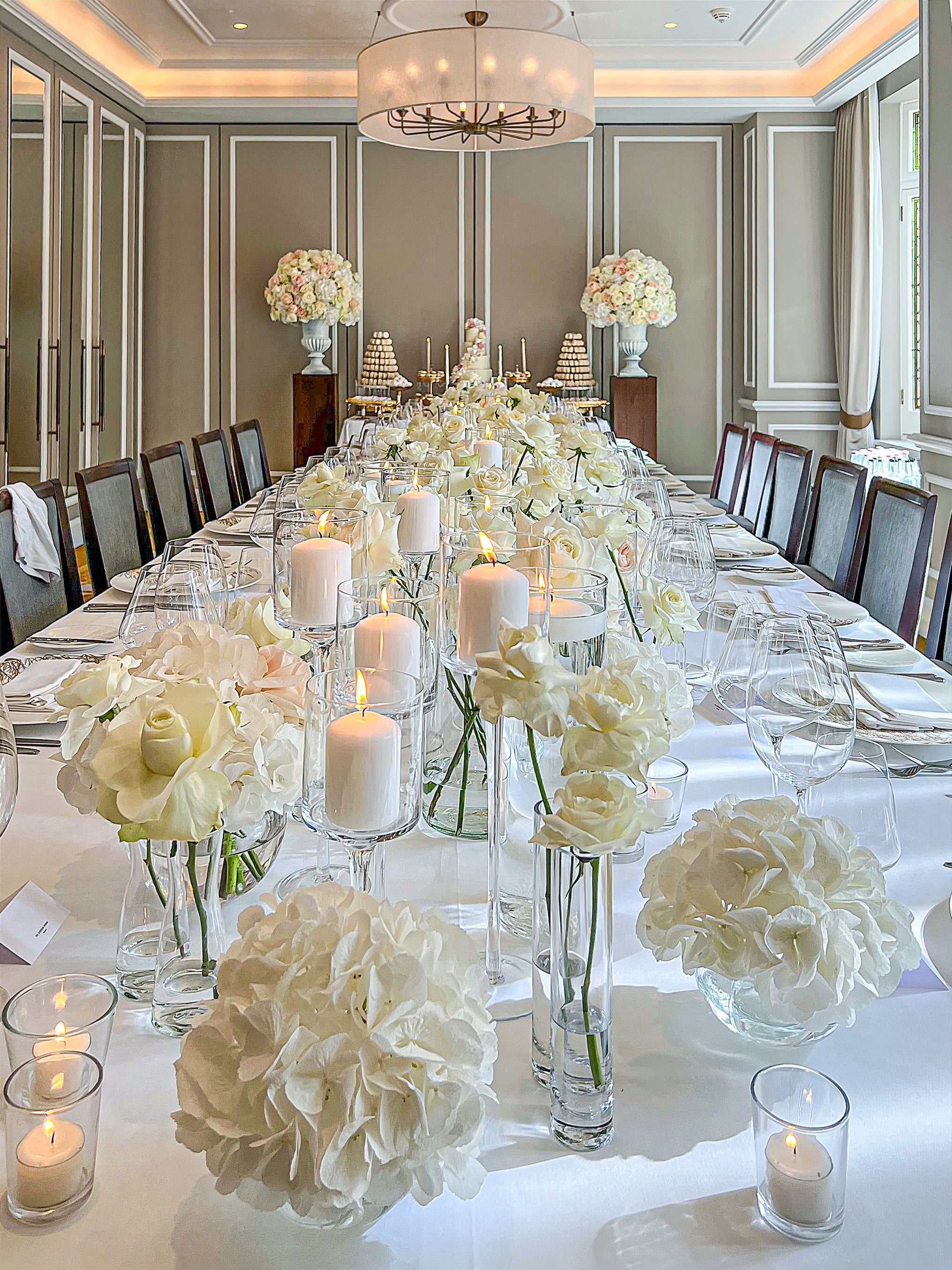 Elegant white bespoke floral tablescape featuring varied height rose arrangements with coordinating pillar candles and crystal glassware in a sophisticated dining room - Amaranté London Event Florist
