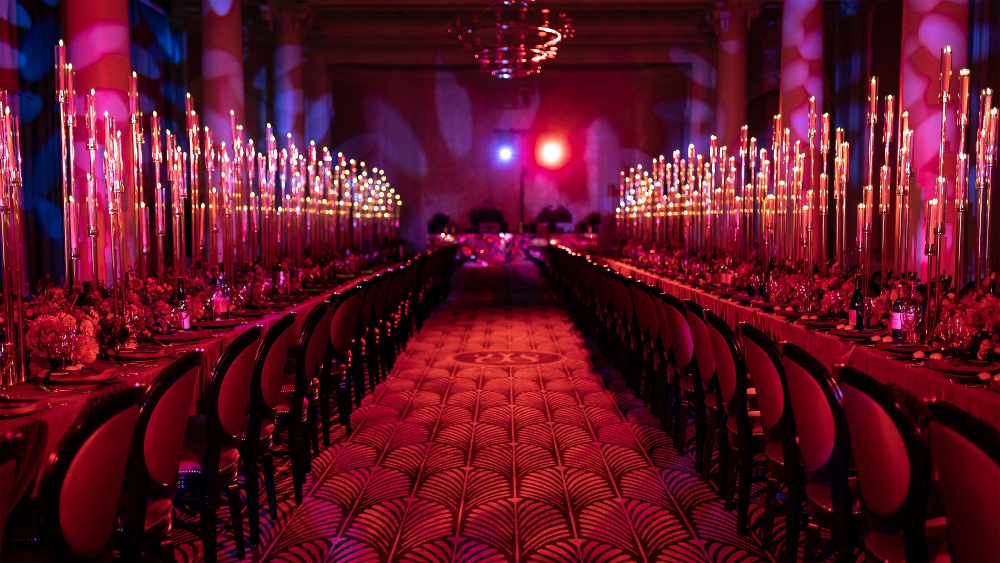 Red-themed wedding event space with towering candle installations and dark floral arrangements creating bold atmospheric lighting - Wedding Planning by Amaranté London