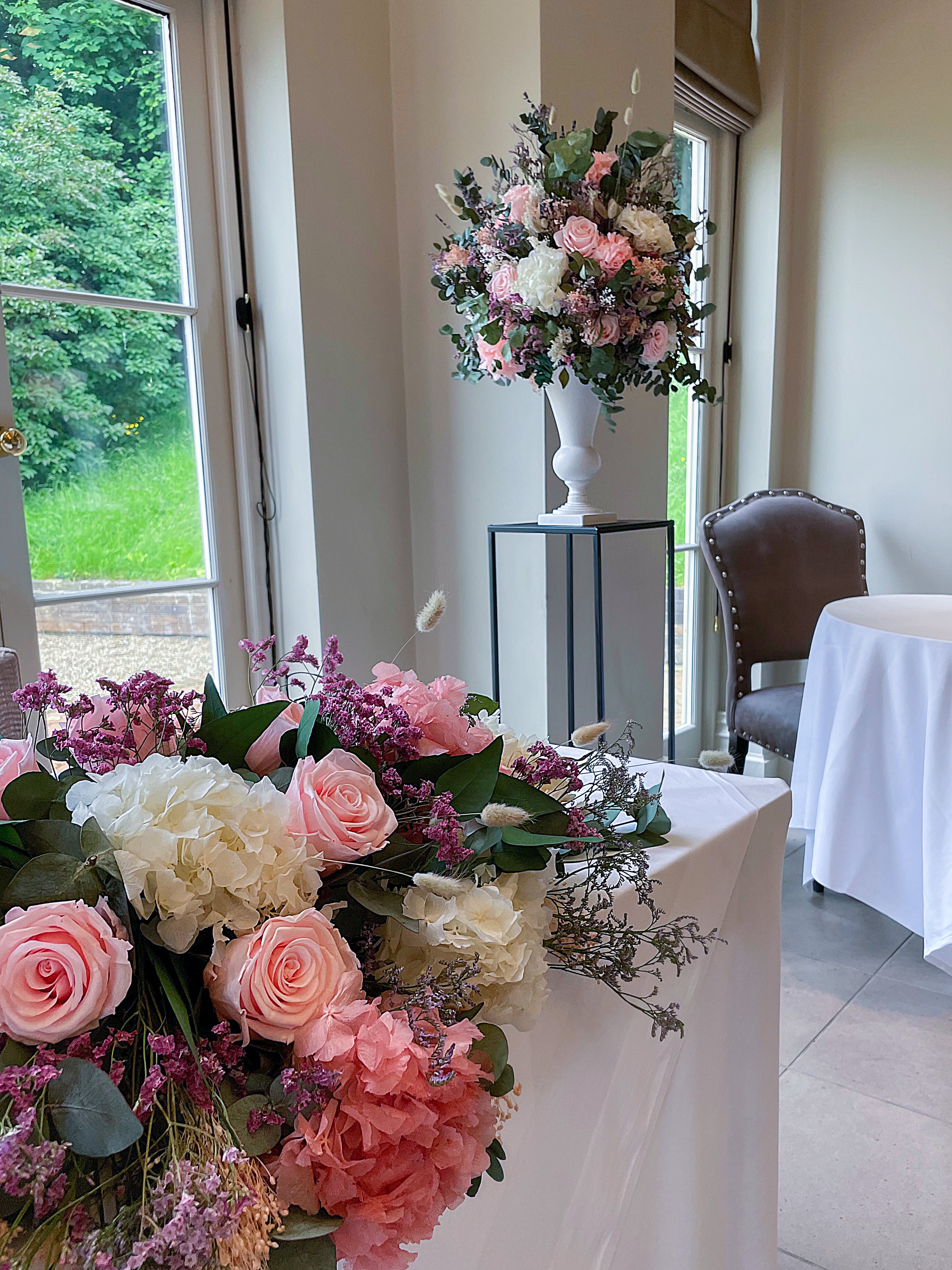 Layered floral display featuring pink roses, white hydrangeas, and purple accents on an elegant console table in a bright interior setting - Amaranté London, sophisticated wedding venue styling