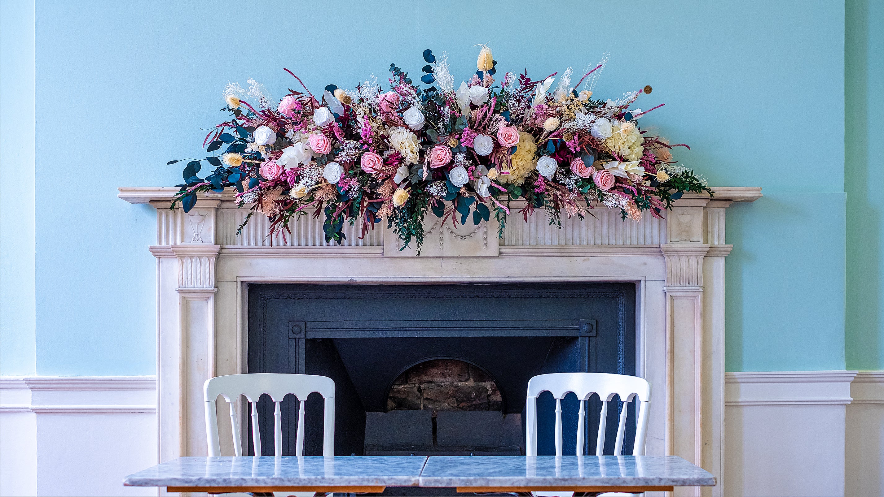 Mantelpiece floral arrangement featuring pink roses, burgundy foliage, and mixed textural elements, creating an abundant display above the fireplace - Amaranté London
