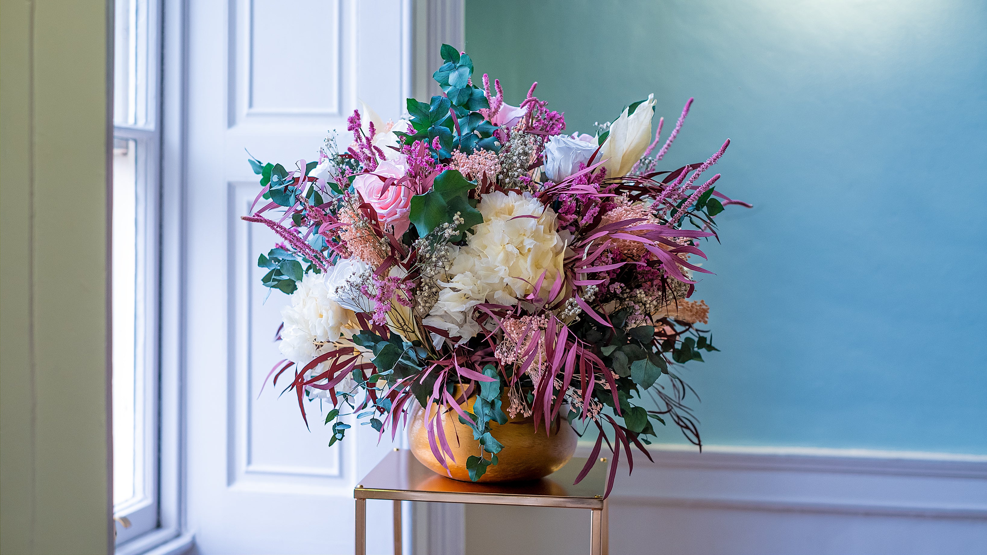Textured mixed floral arrangement featuring white peonies, pink roses, and burgundy foliage in a bronze vessel, creating a rich seasonal display - Amaranté London