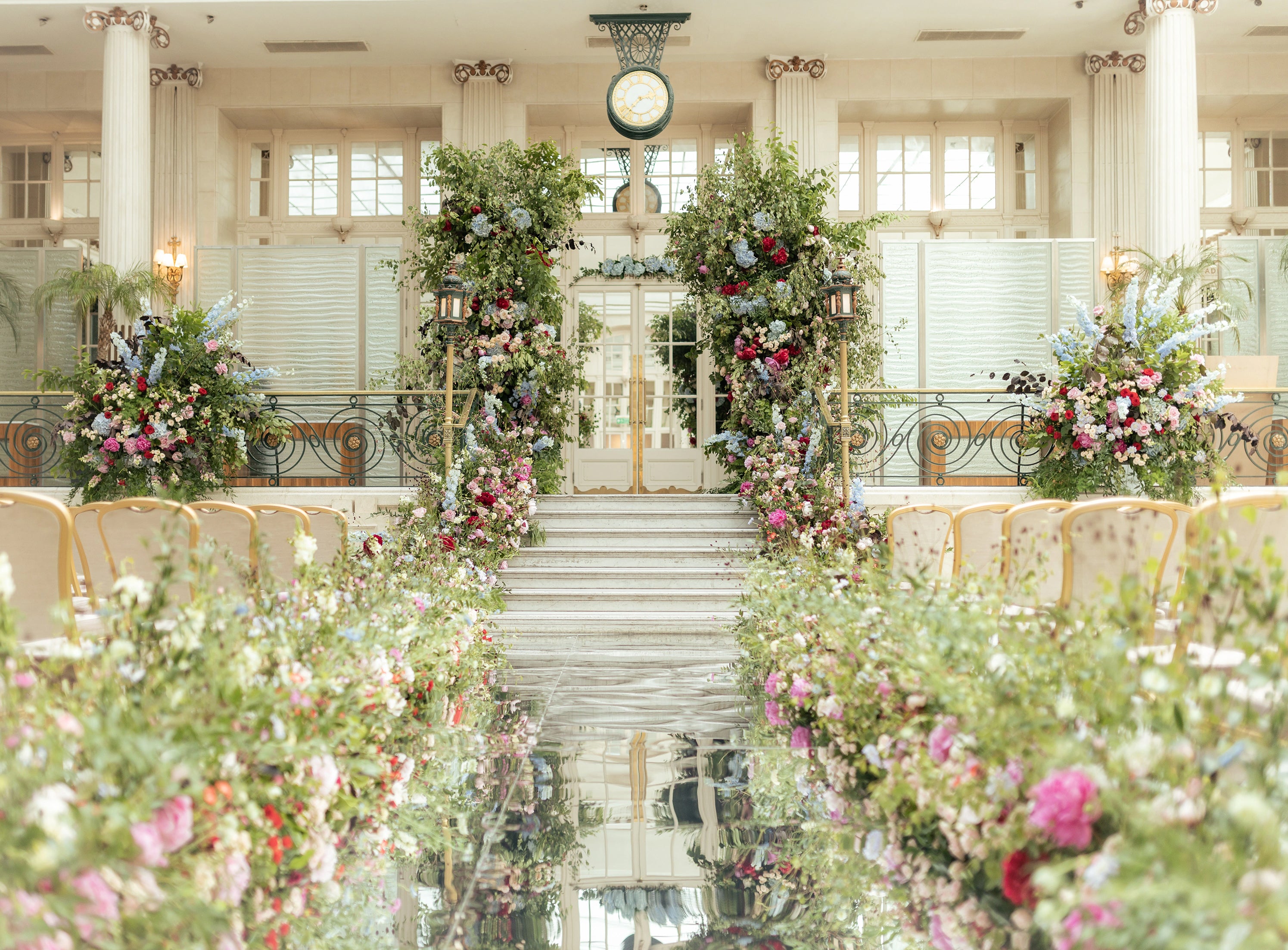Luxury cascading floral archway with mixed seasonal blooms and coordinated aisle arrangements in a classical wedding venue - Floral Design by Amaranté London