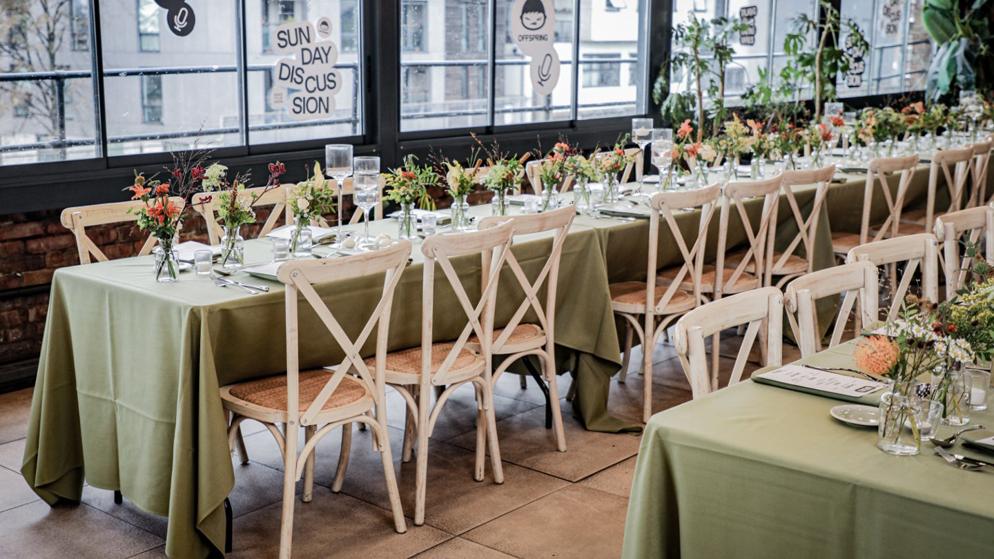 Casual dining setup with natural wildflower arrangements in glass vases on sage green linens in a bright restaurant setting - Amaranté London Event Florist