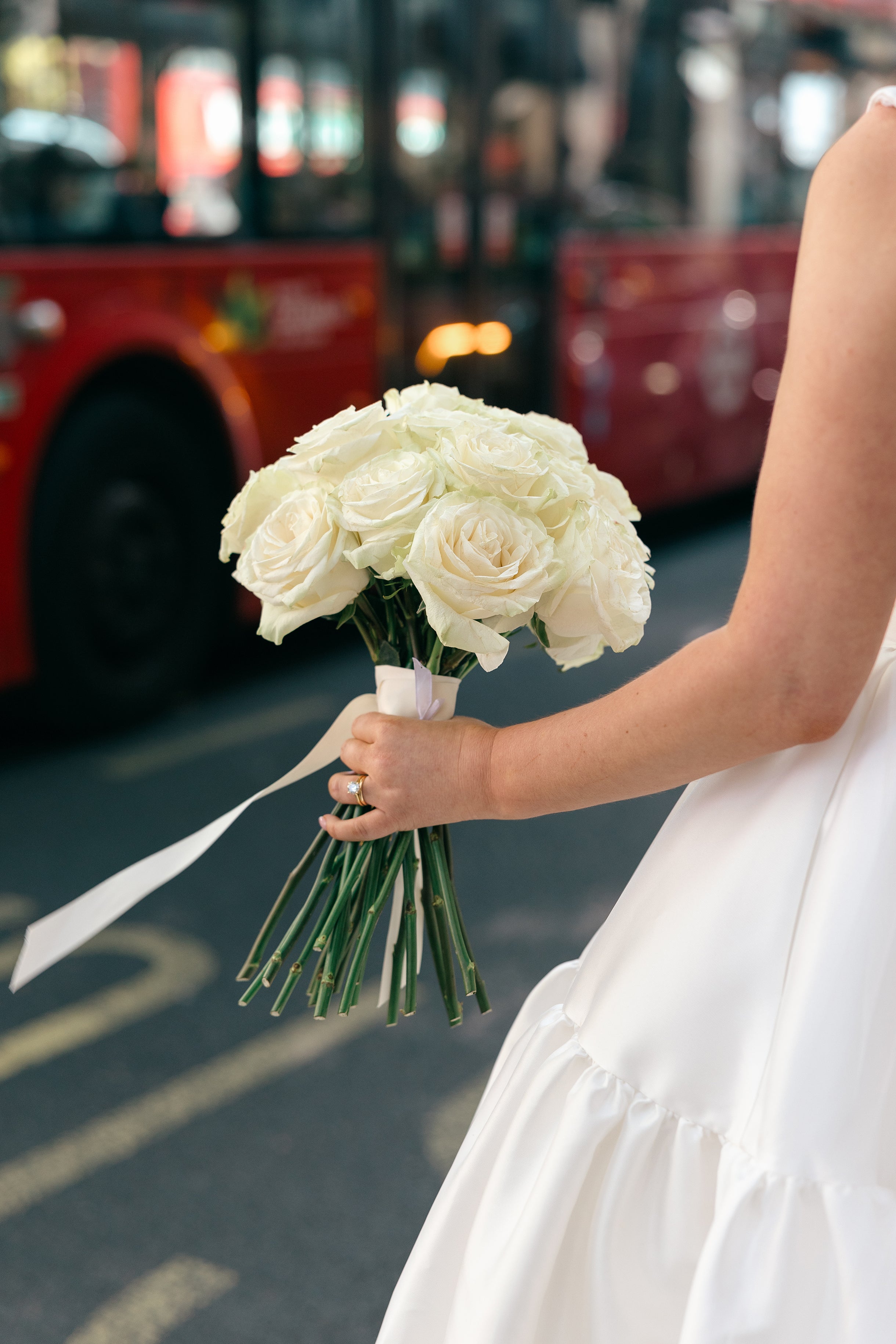 Classic white rose bridal bouquet with clean ribbon wrap held against an urban London backdrop - Amaranté London