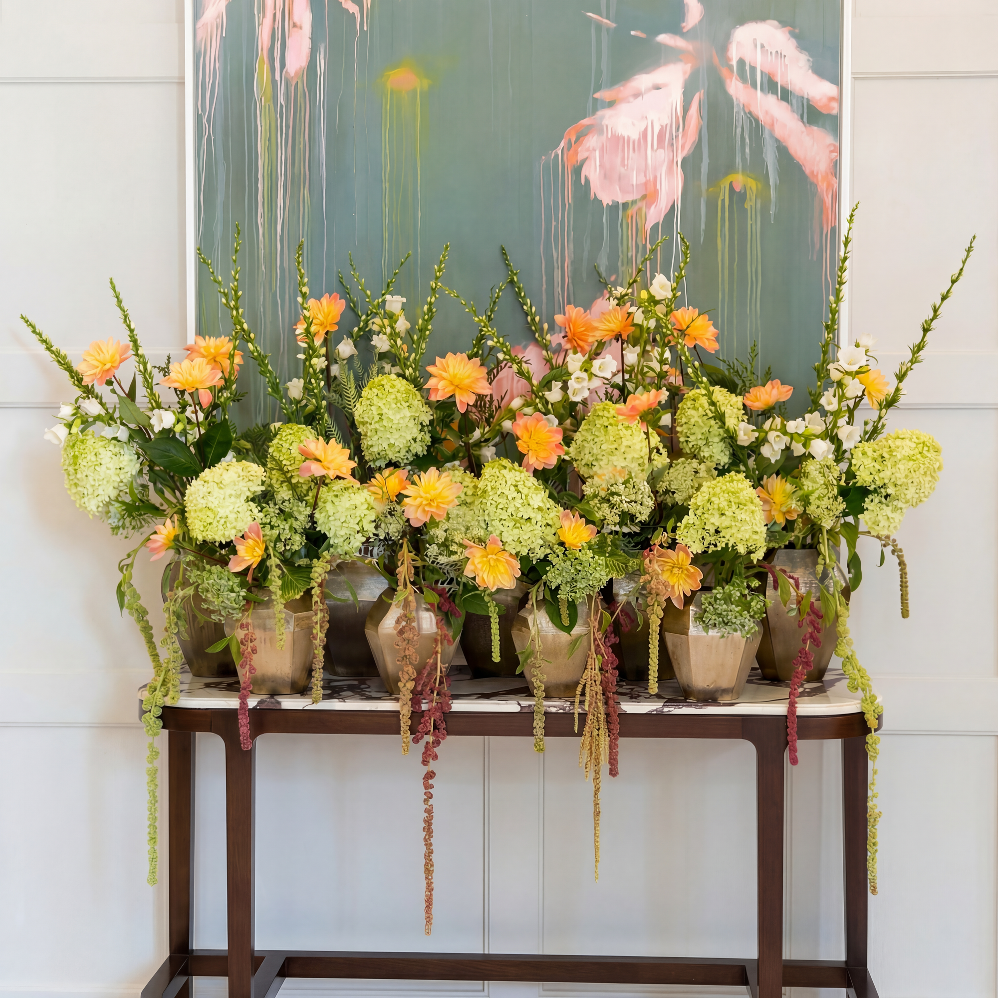 Weekly hotel flower display featuring green hydrangeas, orange gerberas and trailing amaranthus across multiple bronze vases, London hotel flower contract by Amarante London