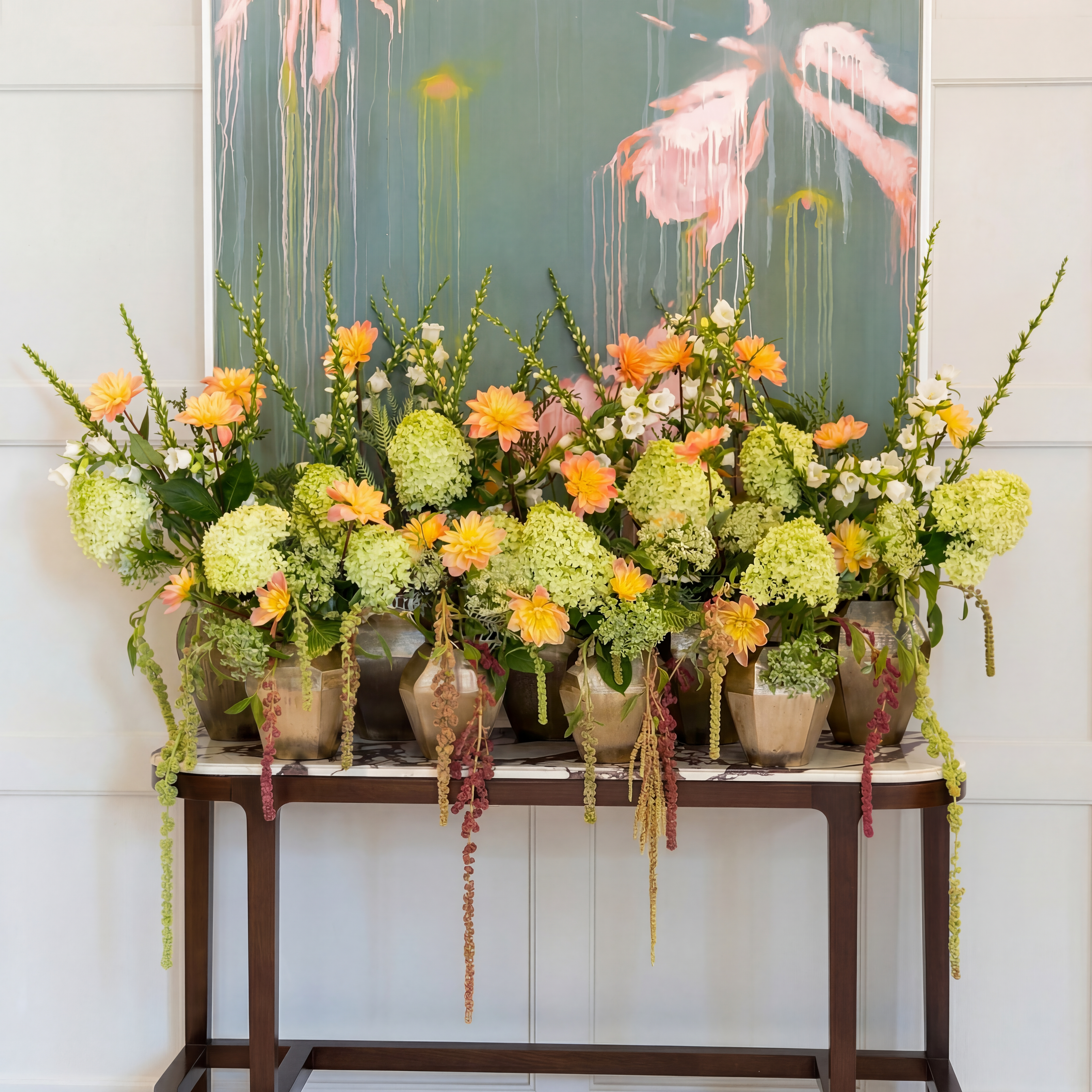 Weekly hotel flower display featuring green hydrangeas, orange gerberas and trailing amaranthus across multiple bronze vases, London hotel flower contract by Amarante London