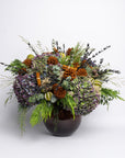 Decorative floral arrangement with greenery and pinecones in a brown vase on a light gray background