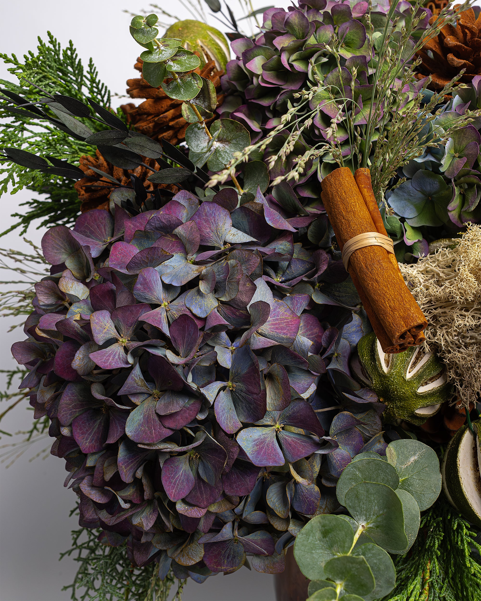 Decorative wreath with purple flowers, greenery, and cinnamon sticks on a white background