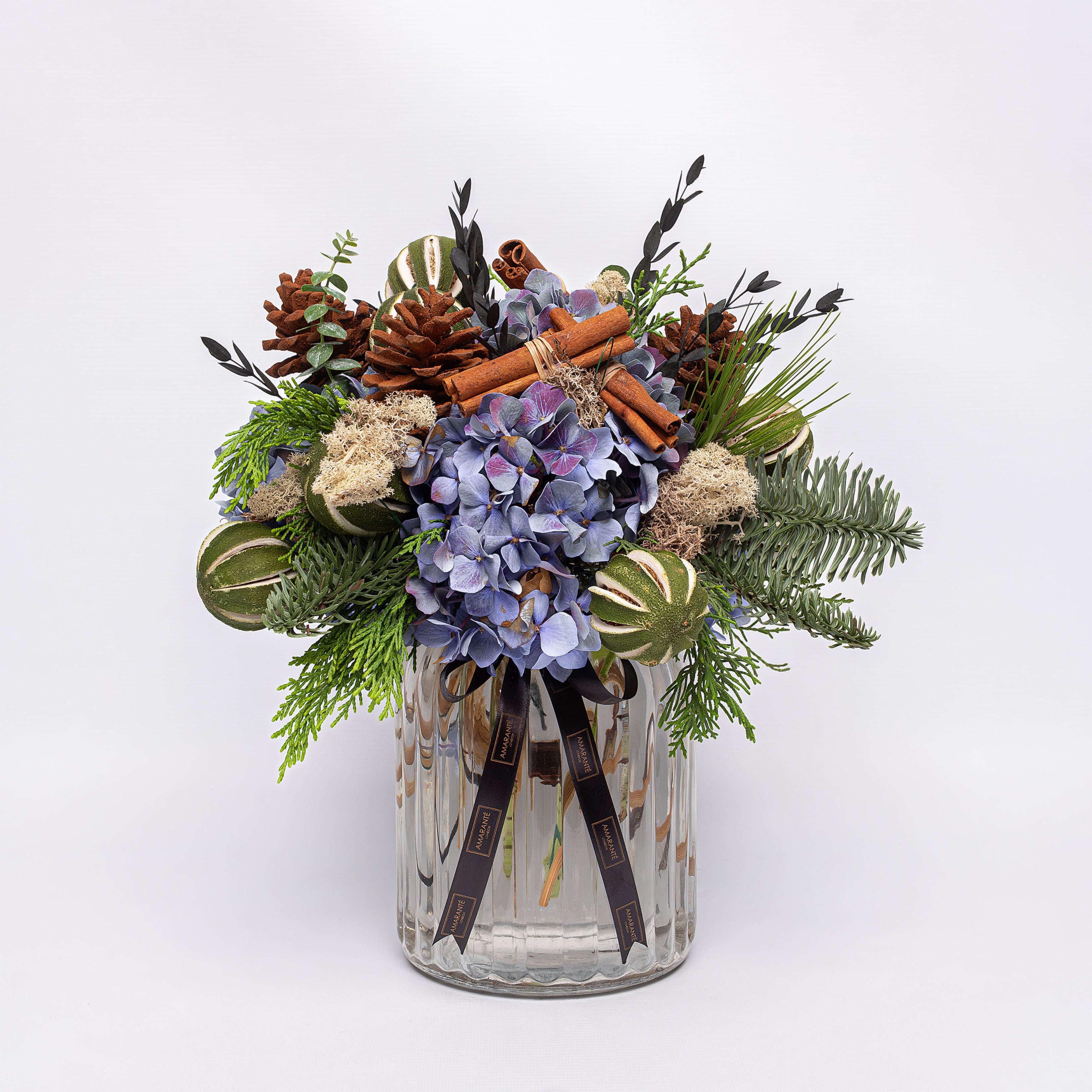 Decorative arrangement with flowers, pinecones, and cinnamon sticks in a clear glass vase on a white background