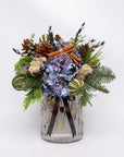 Decorative arrangement with flowers, pinecones, and cinnamon sticks in a clear glass vase on a white background